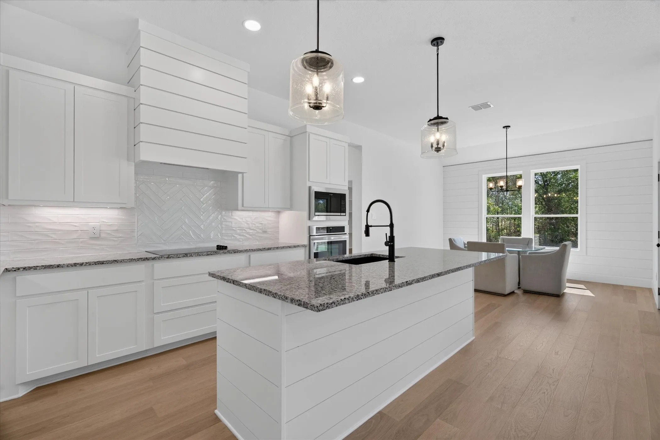 Kitchen featuring a large central island, white shaker cabinetry, granite countertops, and wood-finish flooring