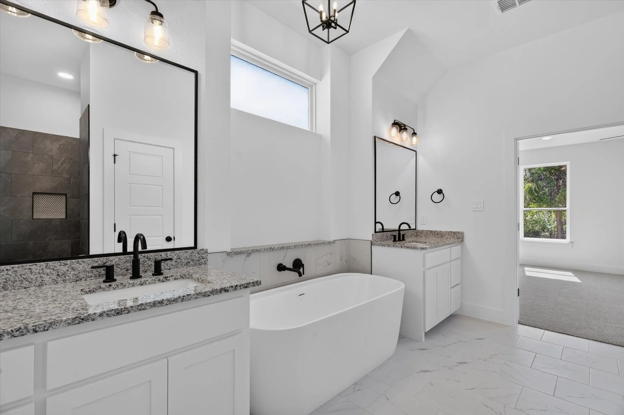 Freestanding soaking tub, dual vanities with granite countertops, black fixtures, and a tiled shower with a niche