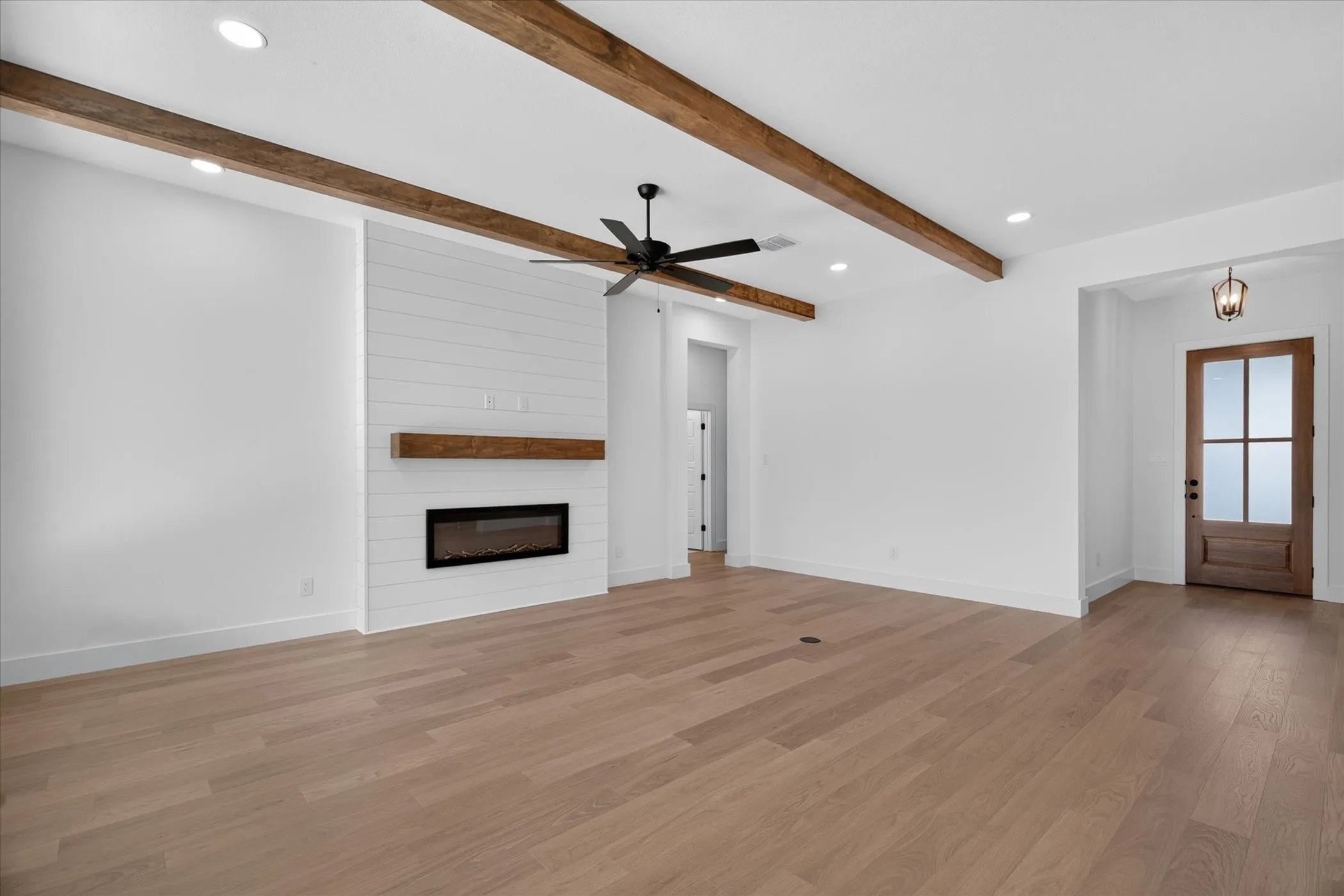 Recessed lighting illuminates wood-finish flooring, a linear electric fireplace with wood mantel, and exposed wood ceiling beams
