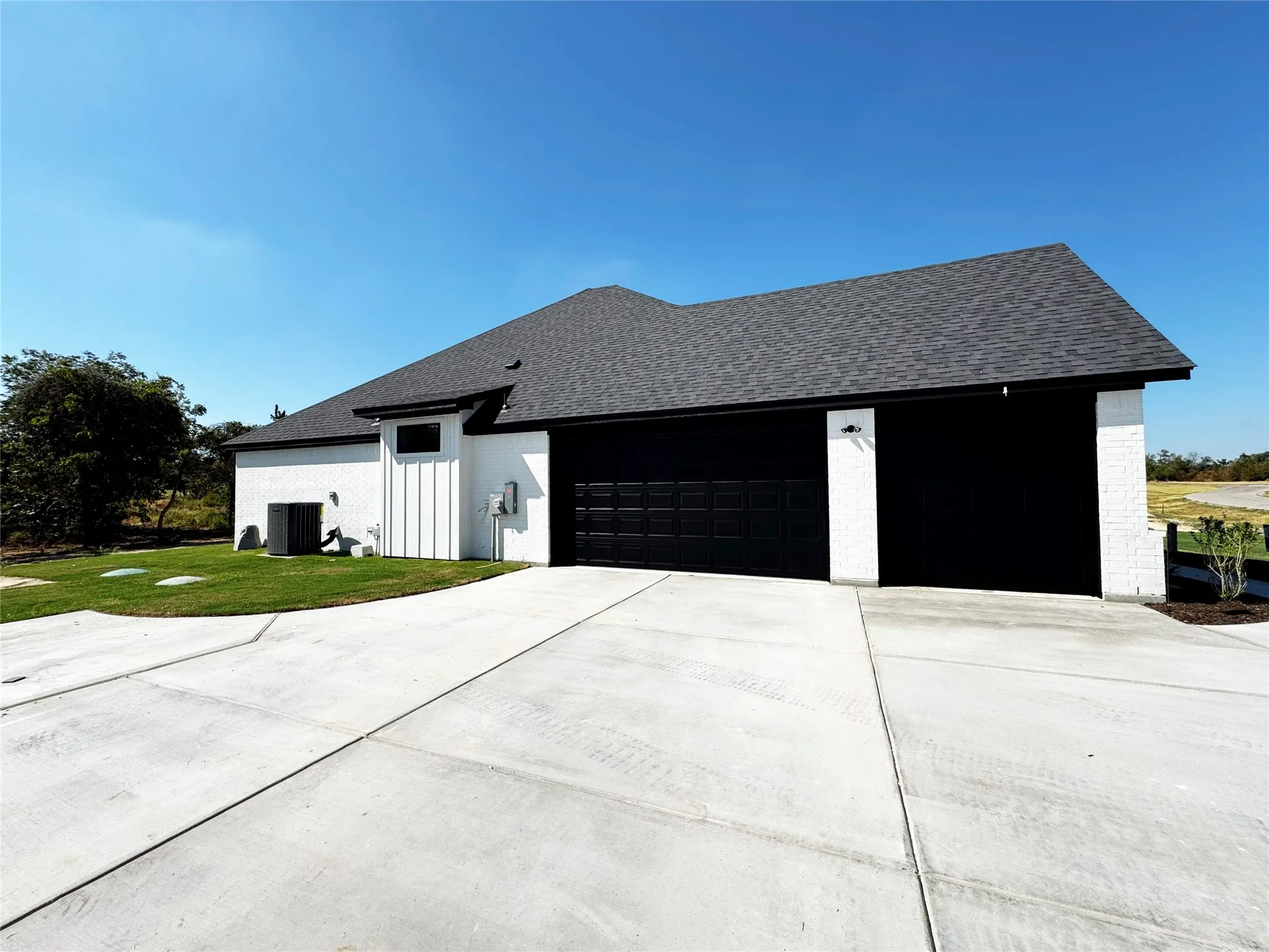 Two-car garage with black doors, white painted brick exterior, dark shingle roof, and a concrete driveway