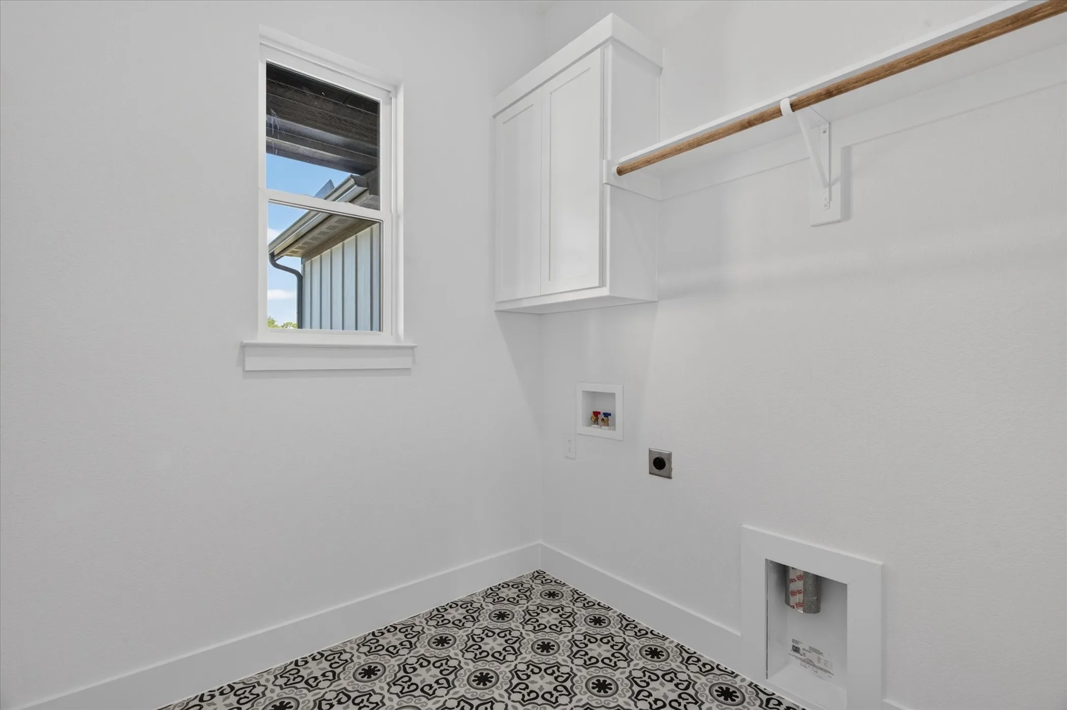 White cabinetry, patterned floor tiles, a single-hung window, and a clothes hanging rod