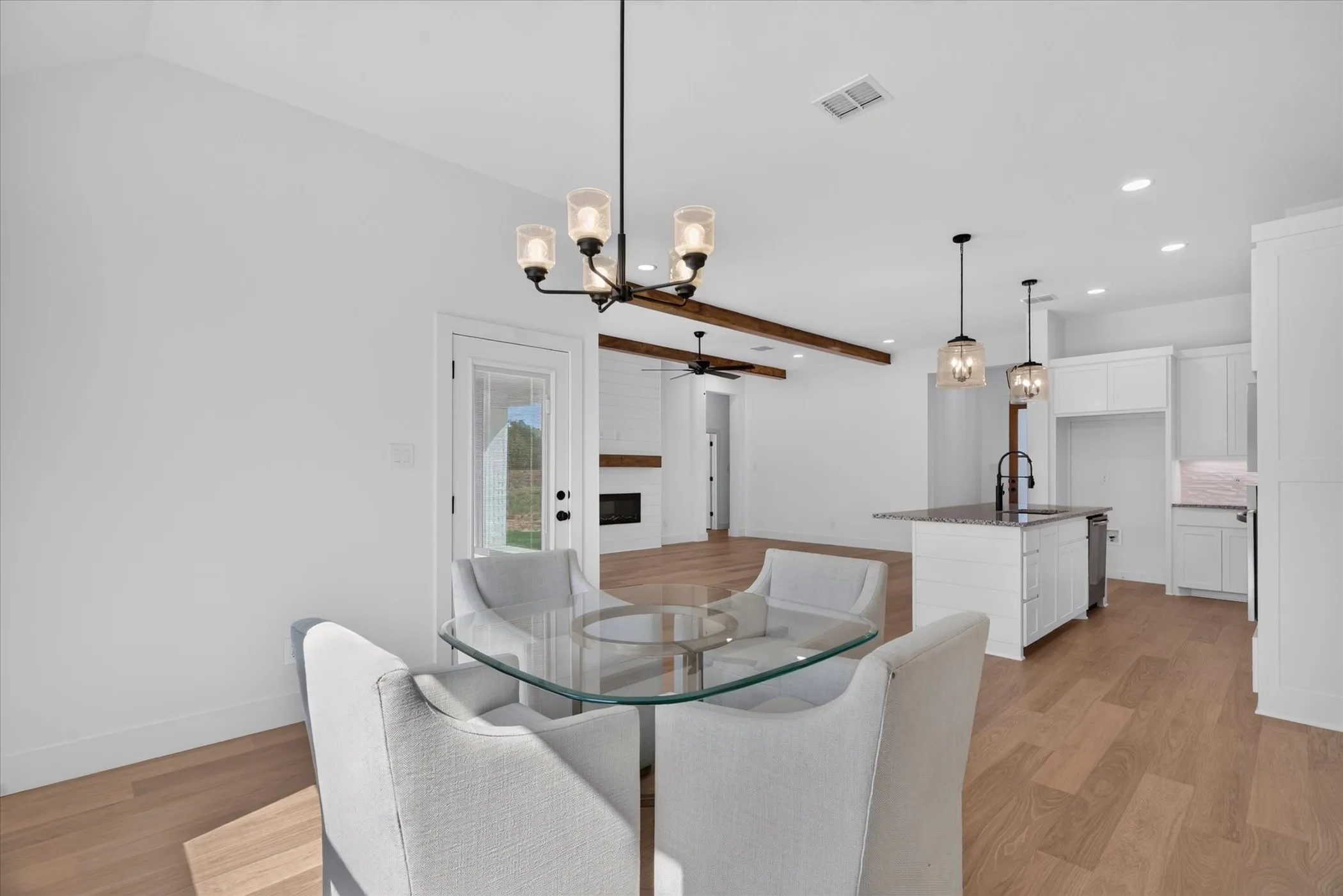 Vaulted ceilings with exposed wood beams, wood-finish flooring, white cabinetry, kitchen island with dark countertop, and a fireplace with wood mantel
