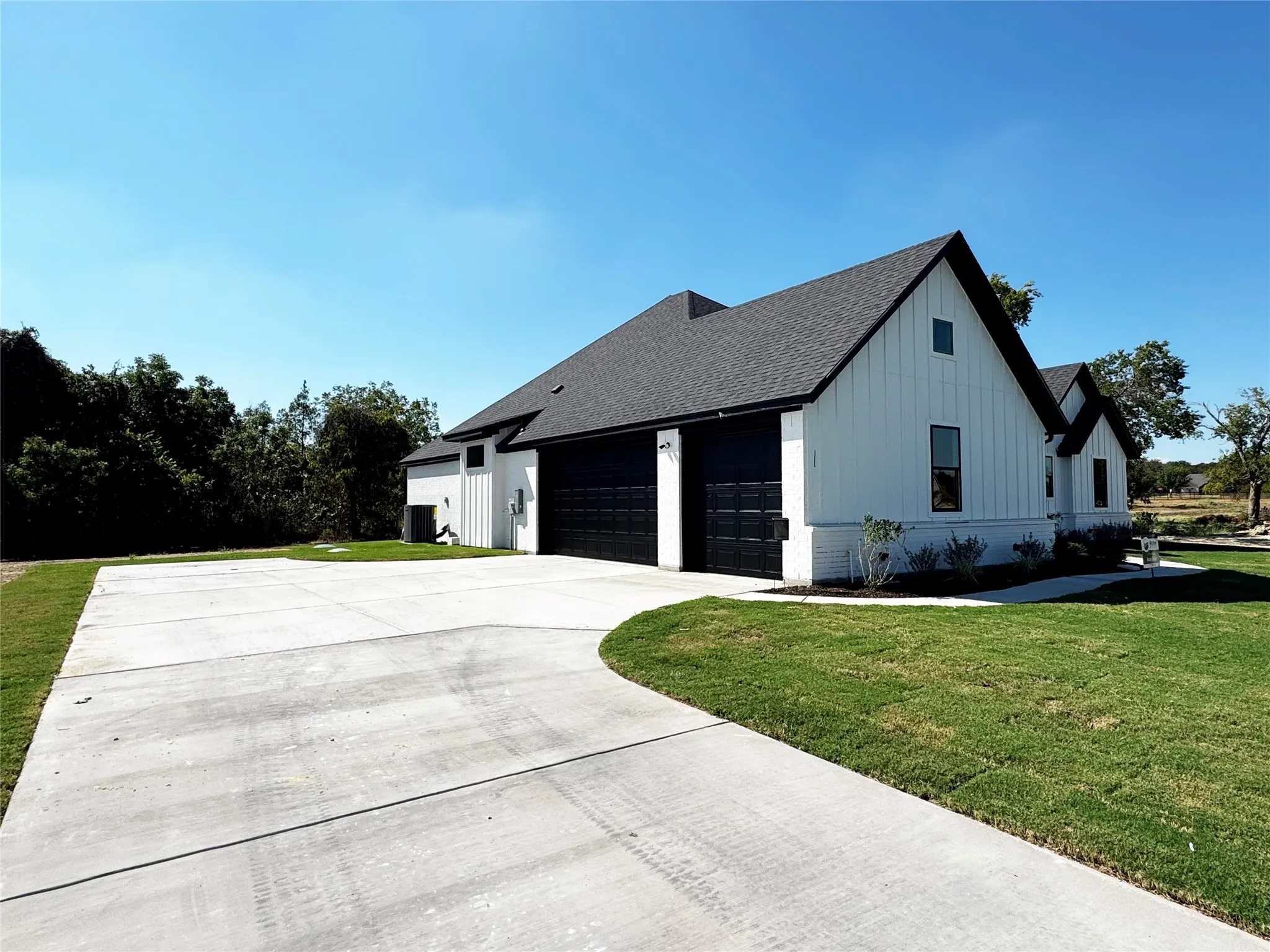 Modern farmhouse exterior with white board and batten siding, dark shingle roof, two black garage doors, and a concrete driveway