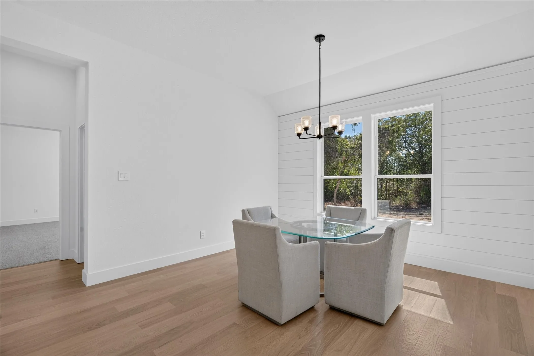 Wood-finish flooring, white shiplap accent wall, dual windows with natural scenery, contemporary chandelier, and white trim throughout