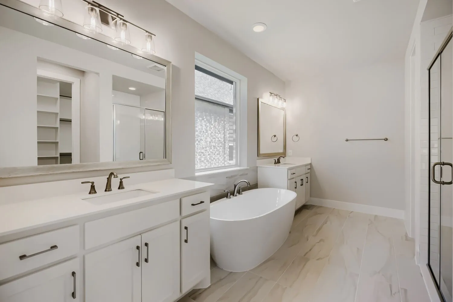 Freestanding soaking tub with a wall-mounted faucet, complemented by dual vanities with white cabinetry and quartz countertops