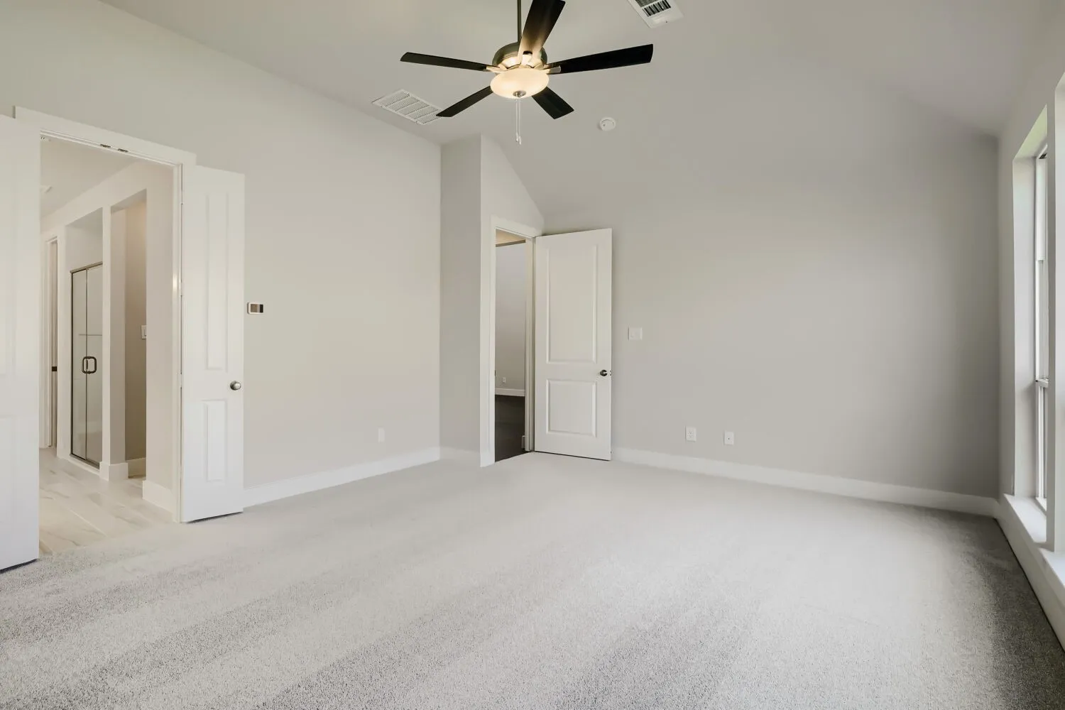 Spacious room featuring vaulted ceilings, light-toned carpeting, and a ceiling fan