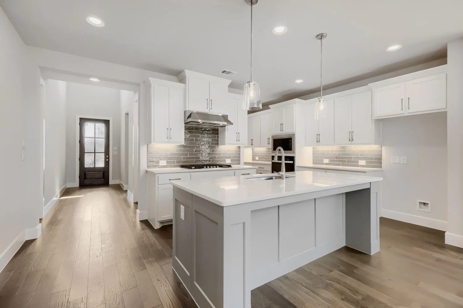 Spacious kitchen featuring an expansive central island with a sink, white cabinetry with under-cabinet lighting, stainless steel appliances, and wood-finish flooring