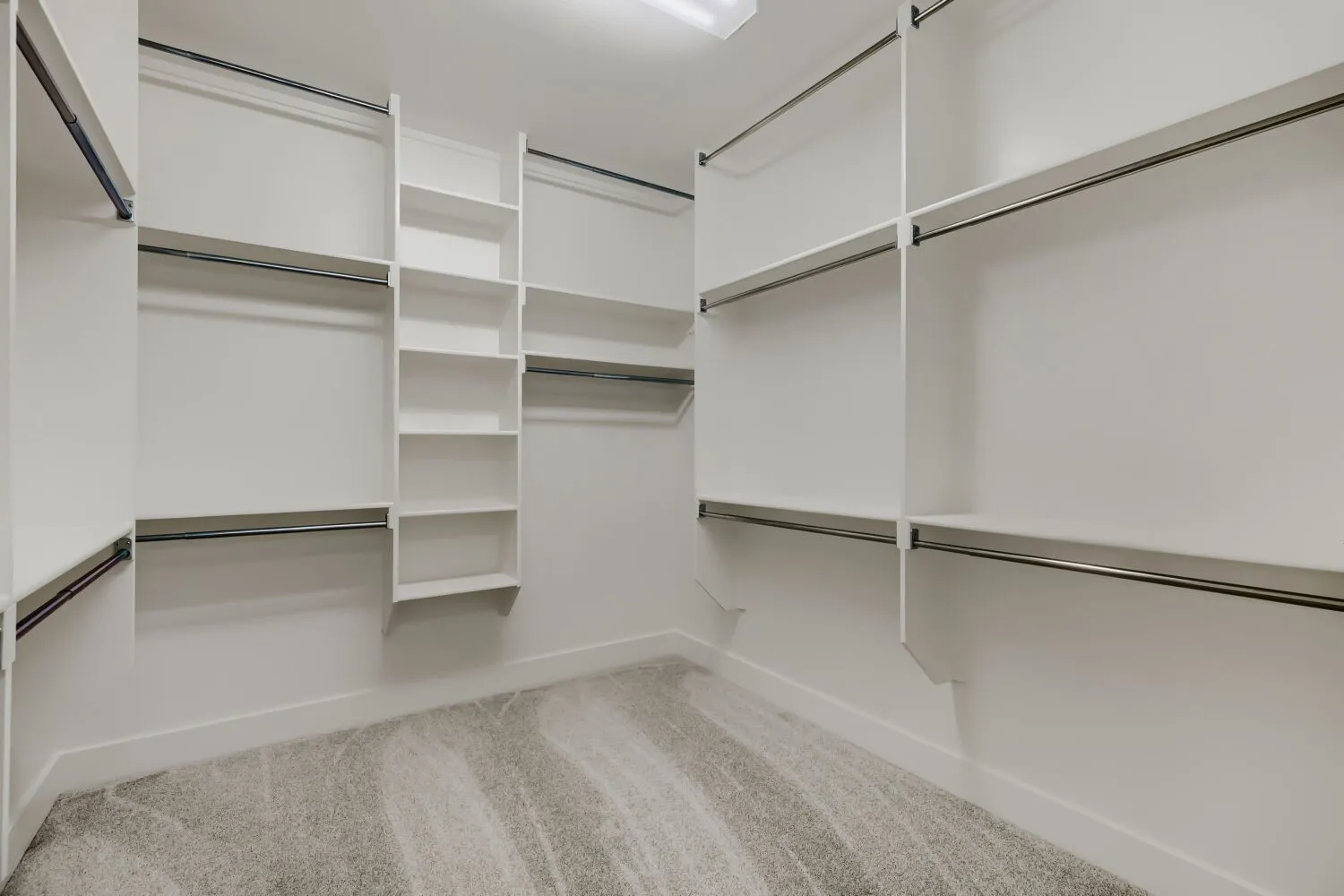 Custom closet system featuring white shelving units, multiple hanging rods, built-in vertical shelving, and recessed ceiling lighting