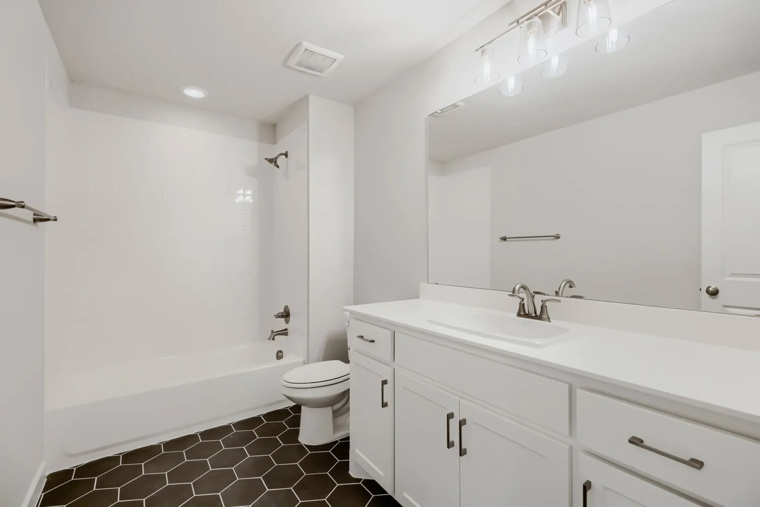 Bathroom featuring hexagonal floor tiles, a white vanity with brushed nickel hardware, a single basin sink, and an integrated tub and shower with white subway tile surround