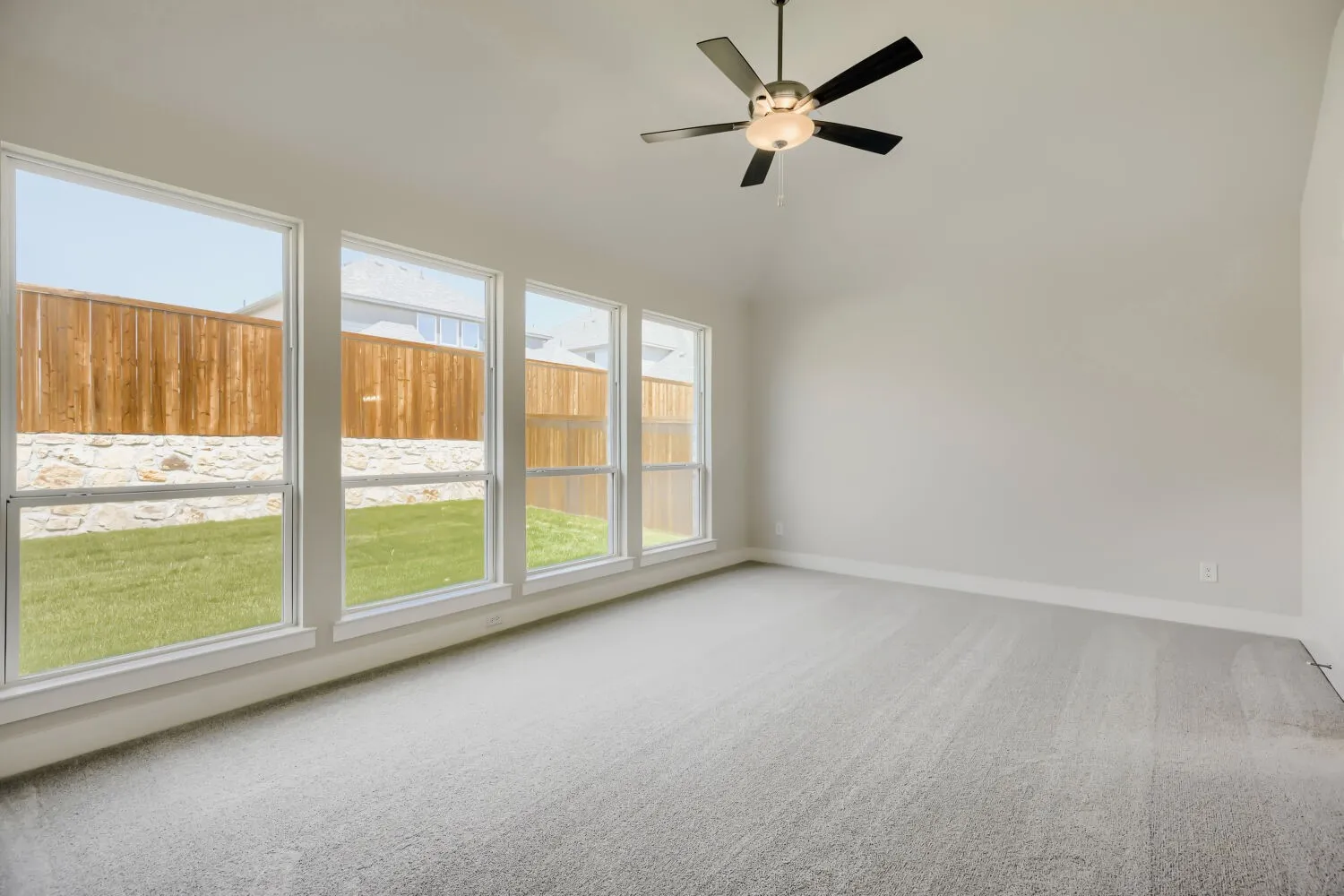 Vaulted ceiling room featuring light gray carpet flooring and multiple large windows