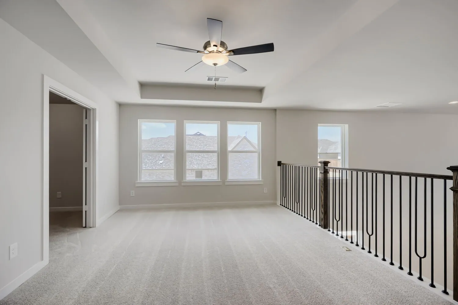 Spacious upper-level room featuring light gray carpeting, a tray ceiling, and a ceiling fan with light fixture