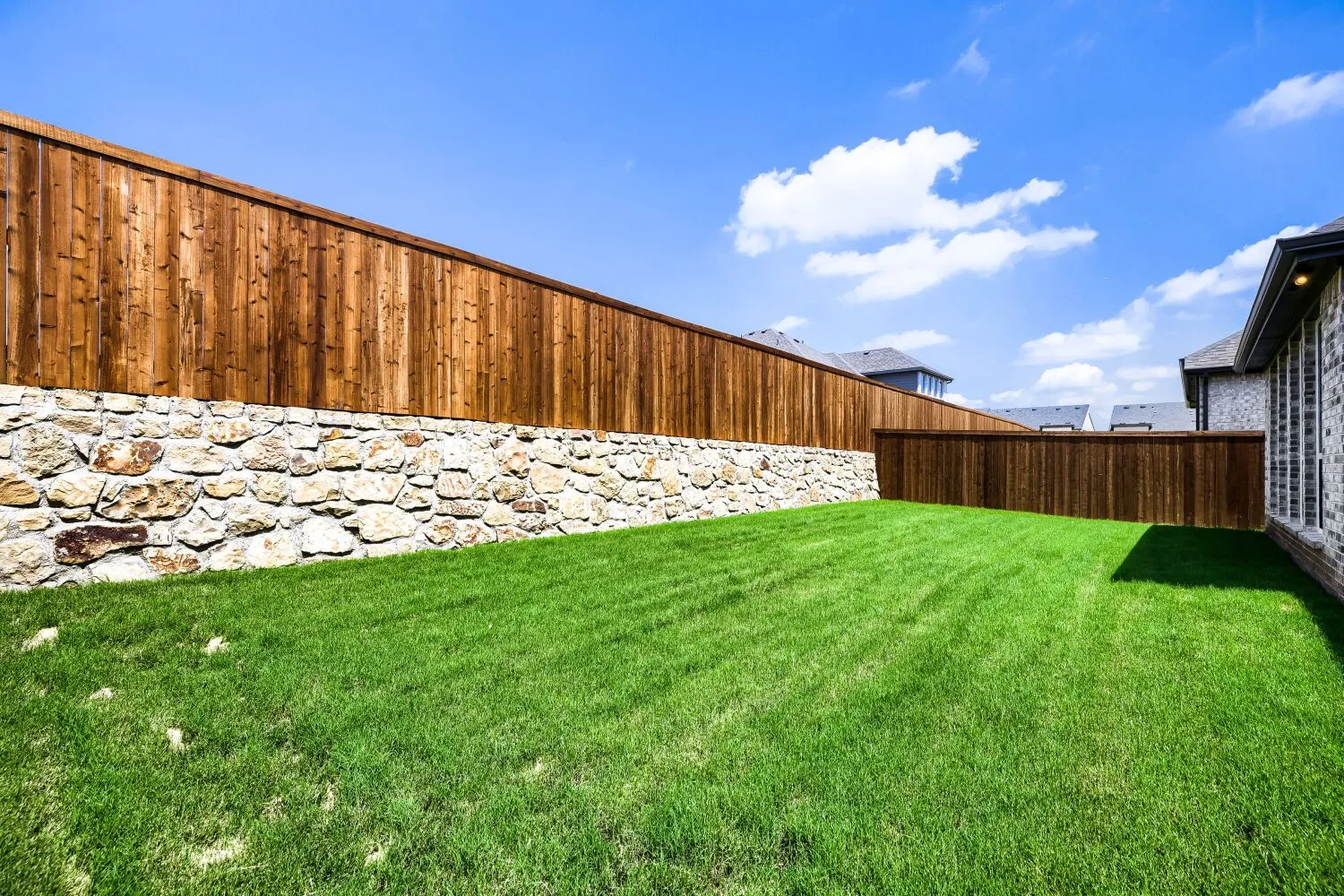 Expansive backyard featuring a manicured lawn, a stone retaining wall, and a full privacy fence
