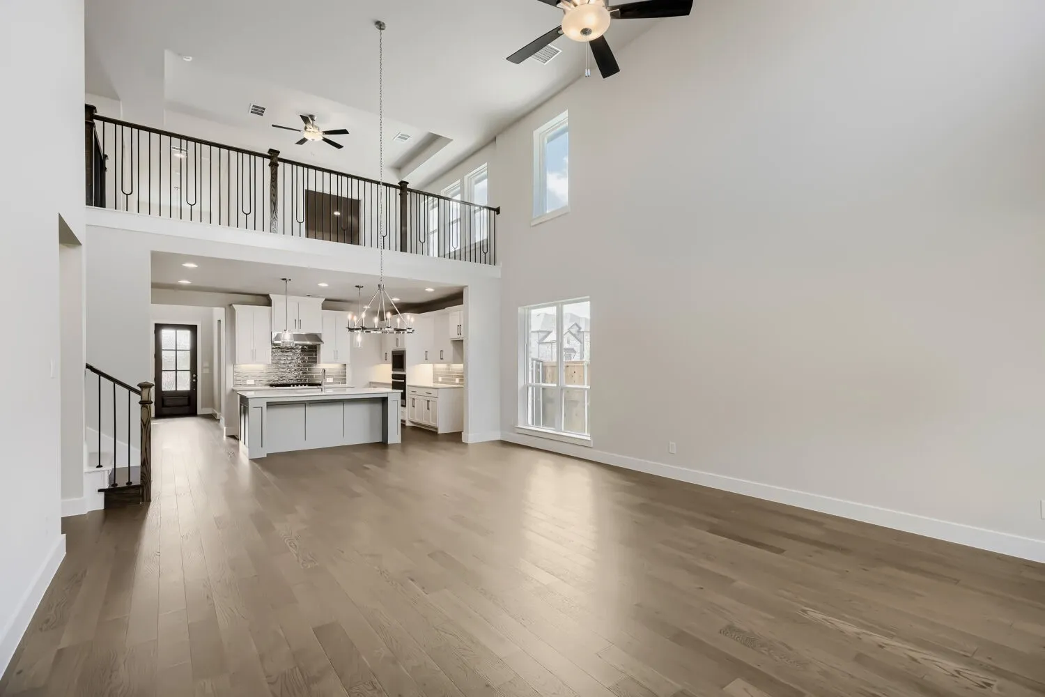 Expansive living area with high ceilings, wood-finish flooring, and multiple windows