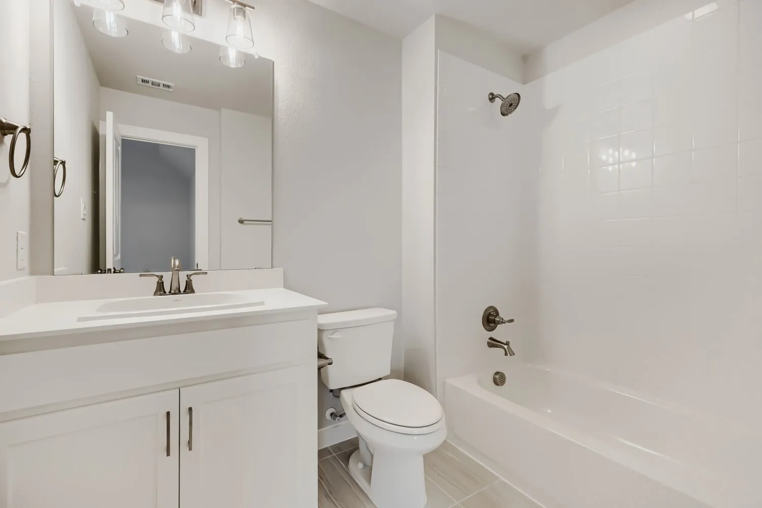Modern bathroom featuring a white vanity with integrated sink, brushed nickel fixtures, a full-sized mirror, and a tub-shower combination with white subway tile surround