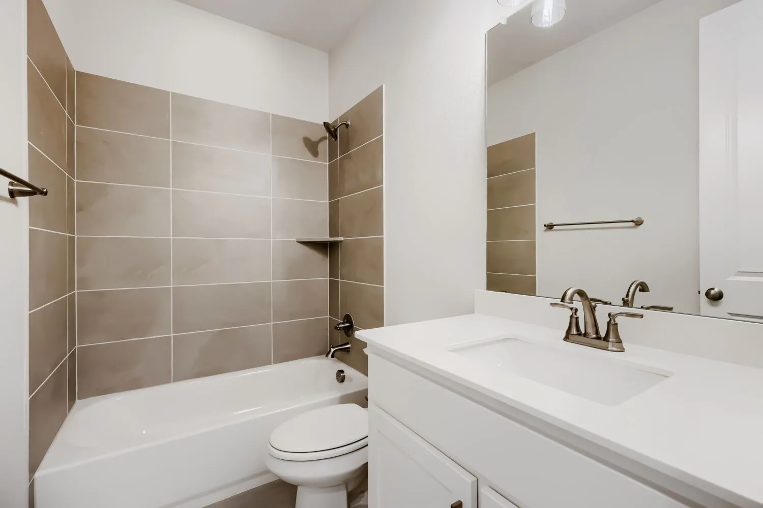 Full bathroom featuring a white vanity with an integrated sink, a large wall-mounted mirror, and a bathtub with tile surround extending to the ceiling