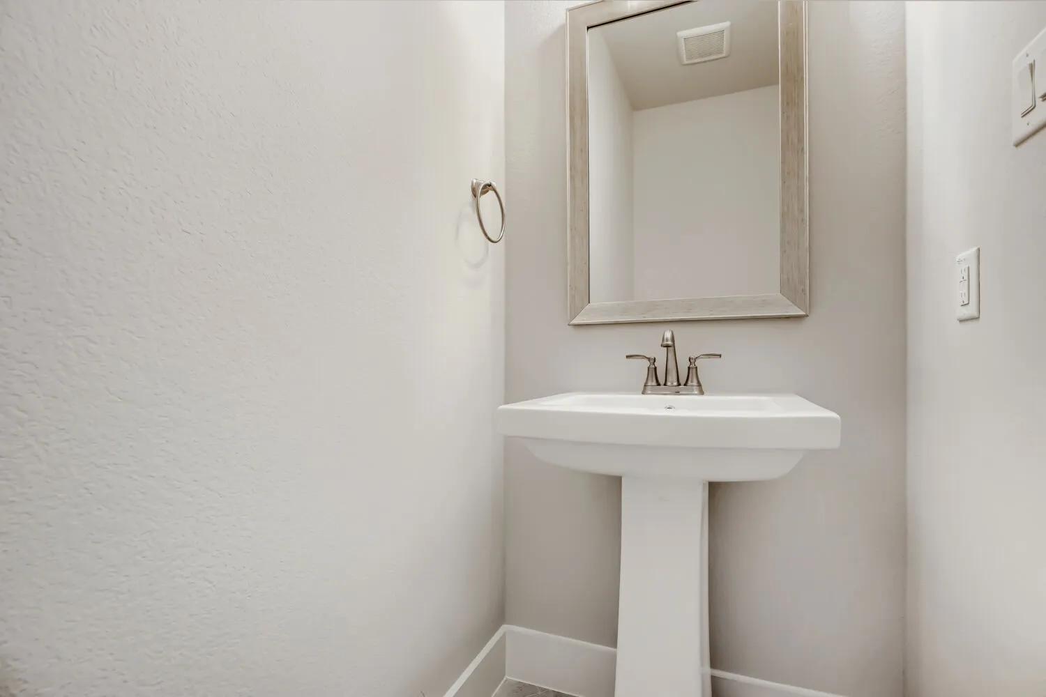 Pedestal sink with brushed nickel faucet, framed mirror, and a wall-mounted towel ring
