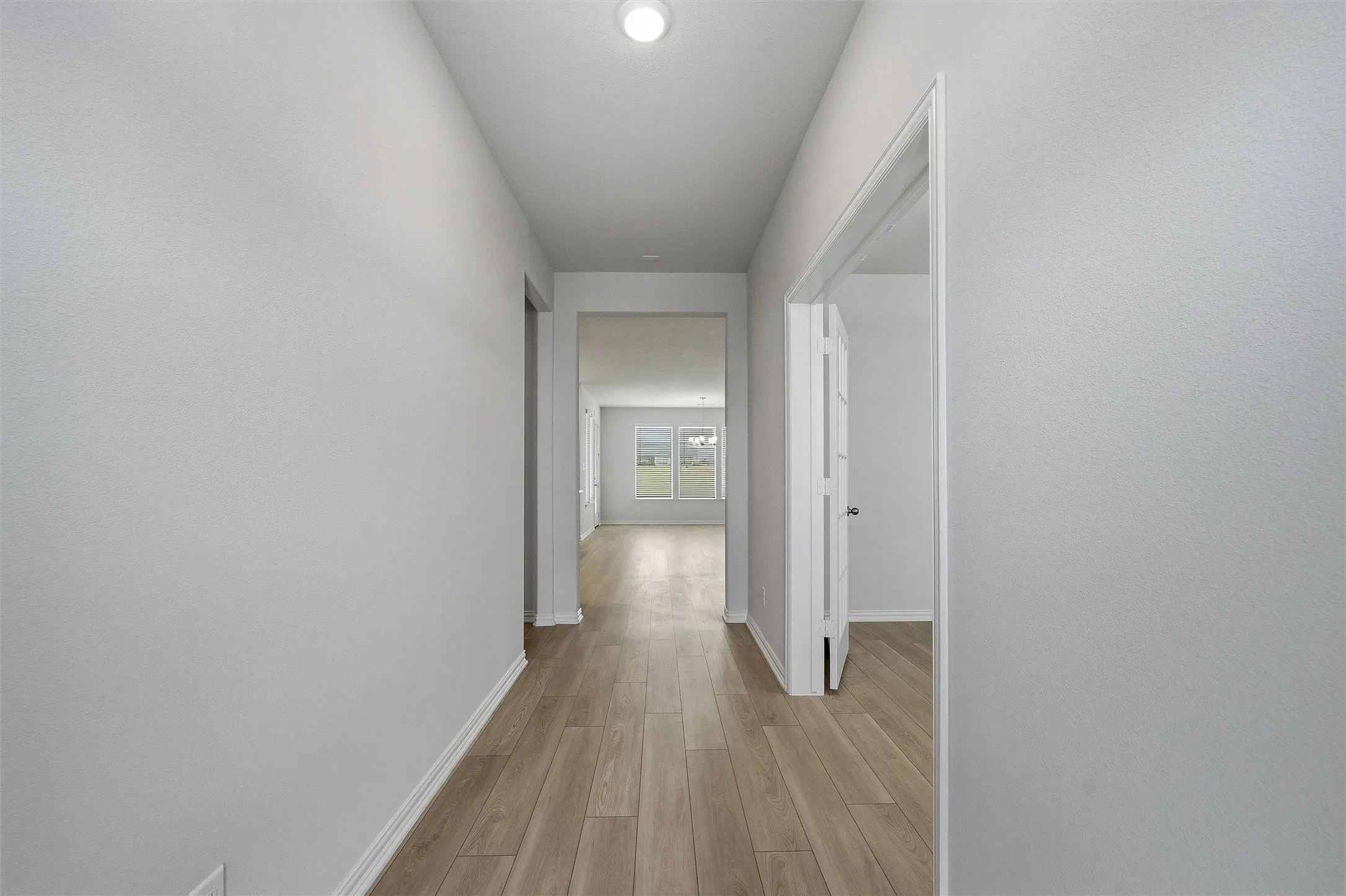 Neutral-toned hallway featuring wood-finish flooring, white baseboards, and overhead lighting