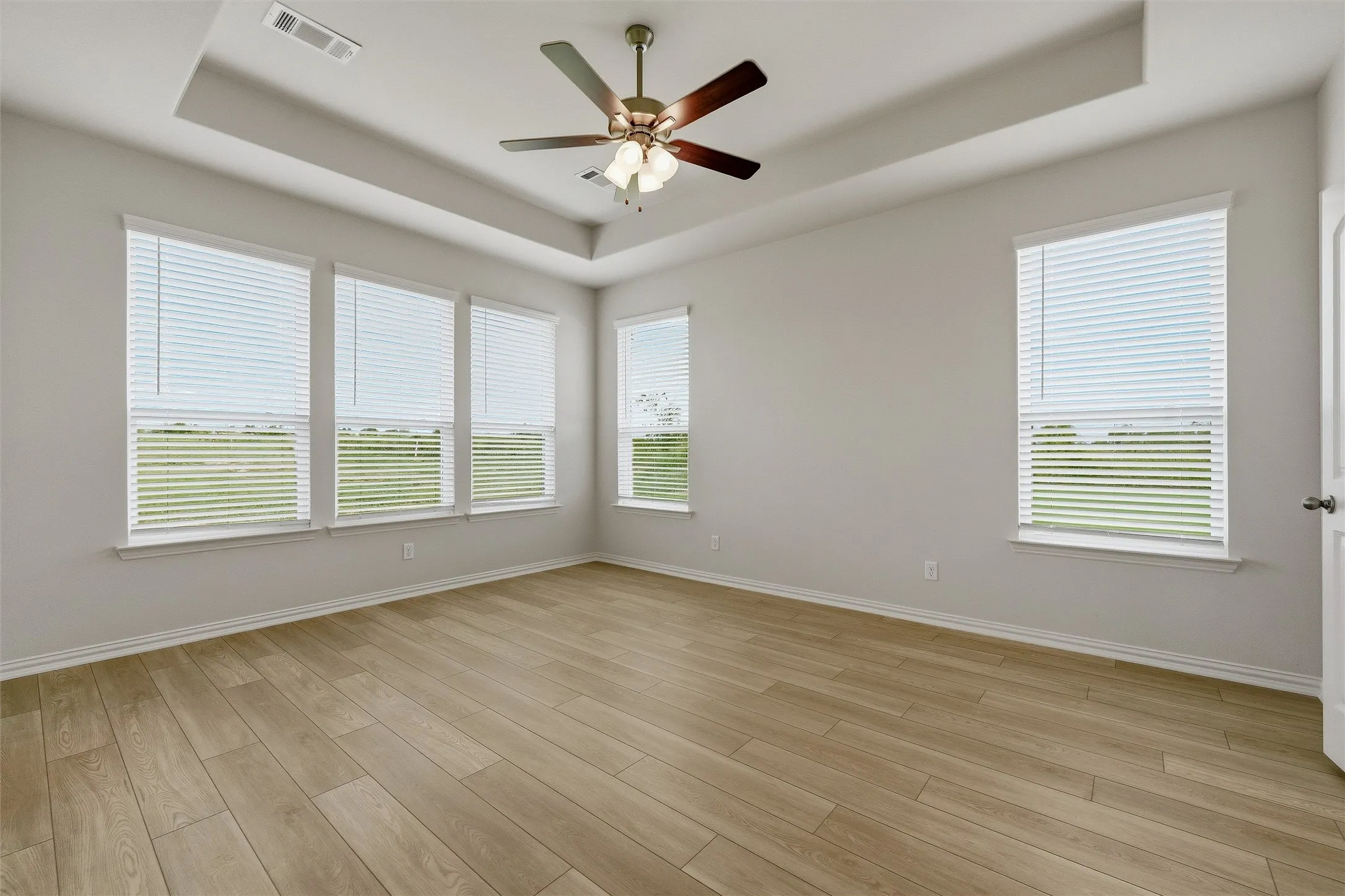 Spacious room featuring wood-finish flooring and a tray ceiling with a ceiling fan