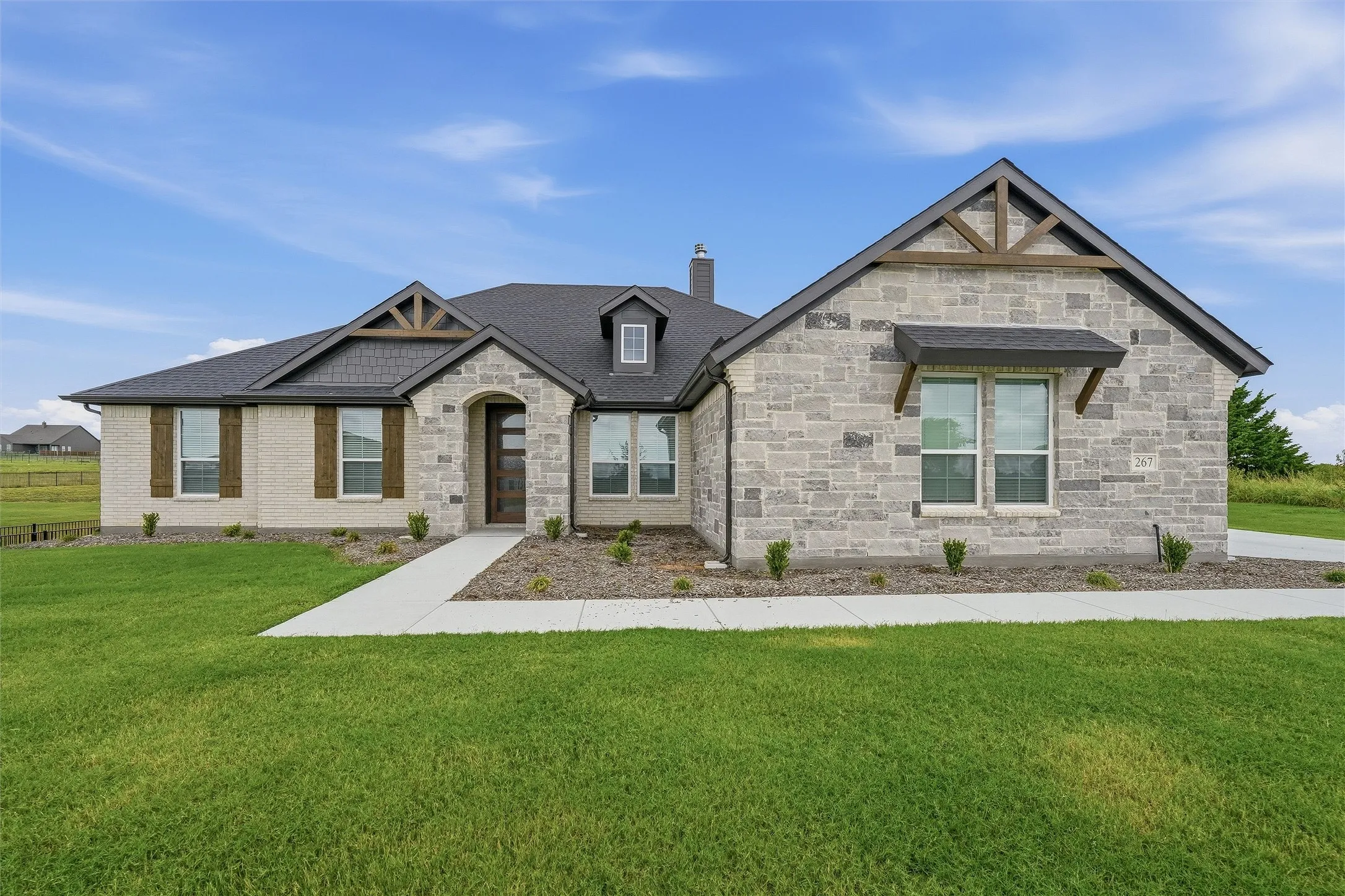 Stone and brick exterior featuring a dark asphalt shingle roof, decorative wooden gables, and a prominent front entry with an arched stone surround