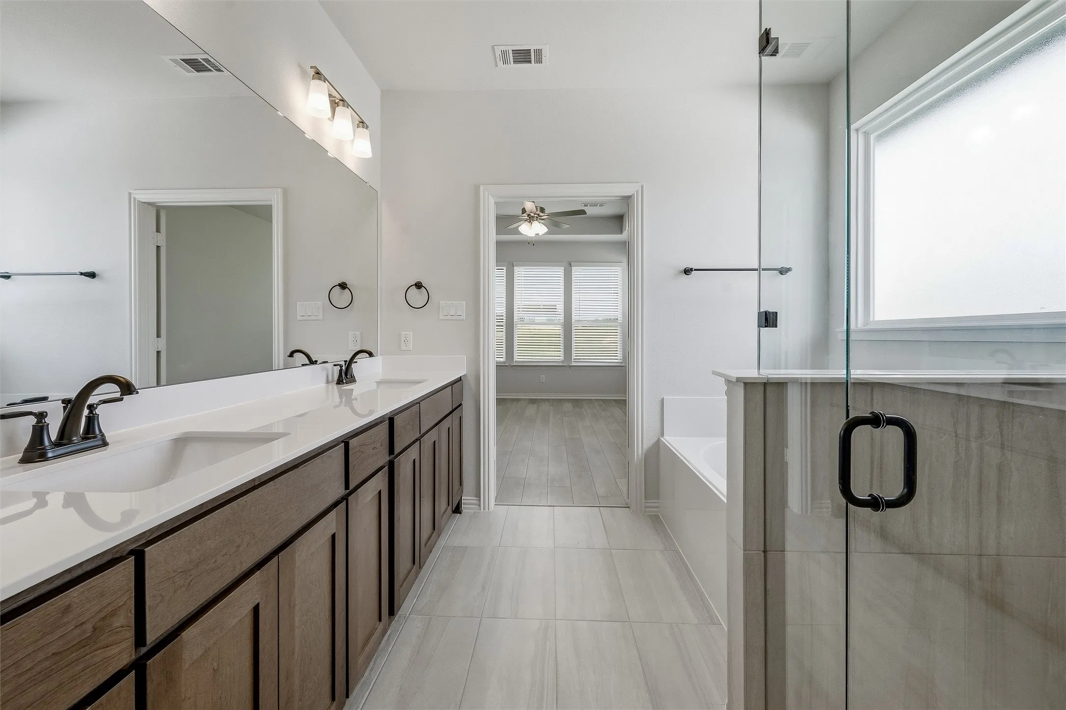 Spacious bathroom featuring a dual vanity with dark wood-finish cabinetry, white countertops, and matte black fixtures