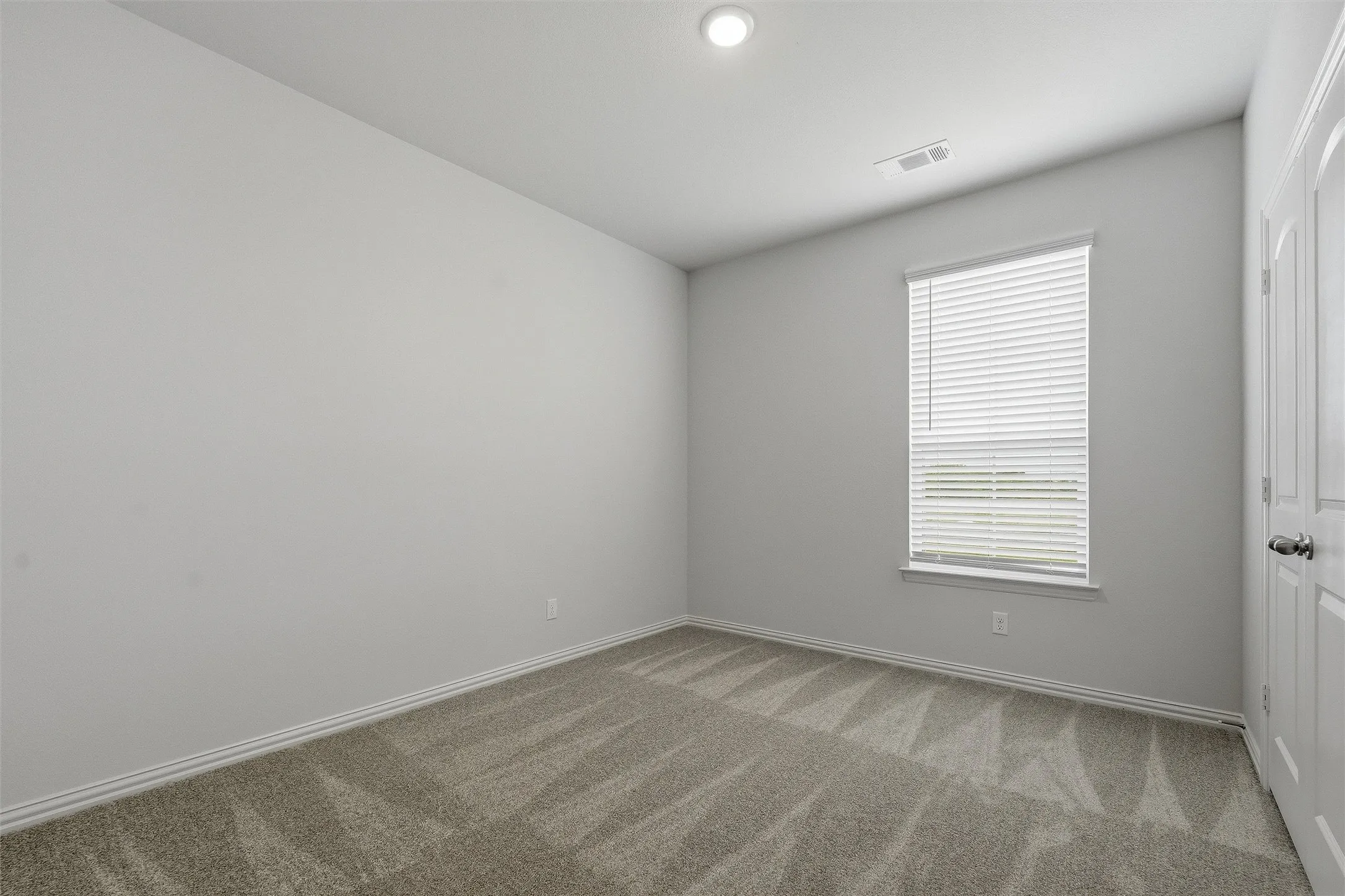 Carpeted room featuring a single window with horizontal blinds, recessed ceiling lighting, and a paneled door with a dark-finish knob