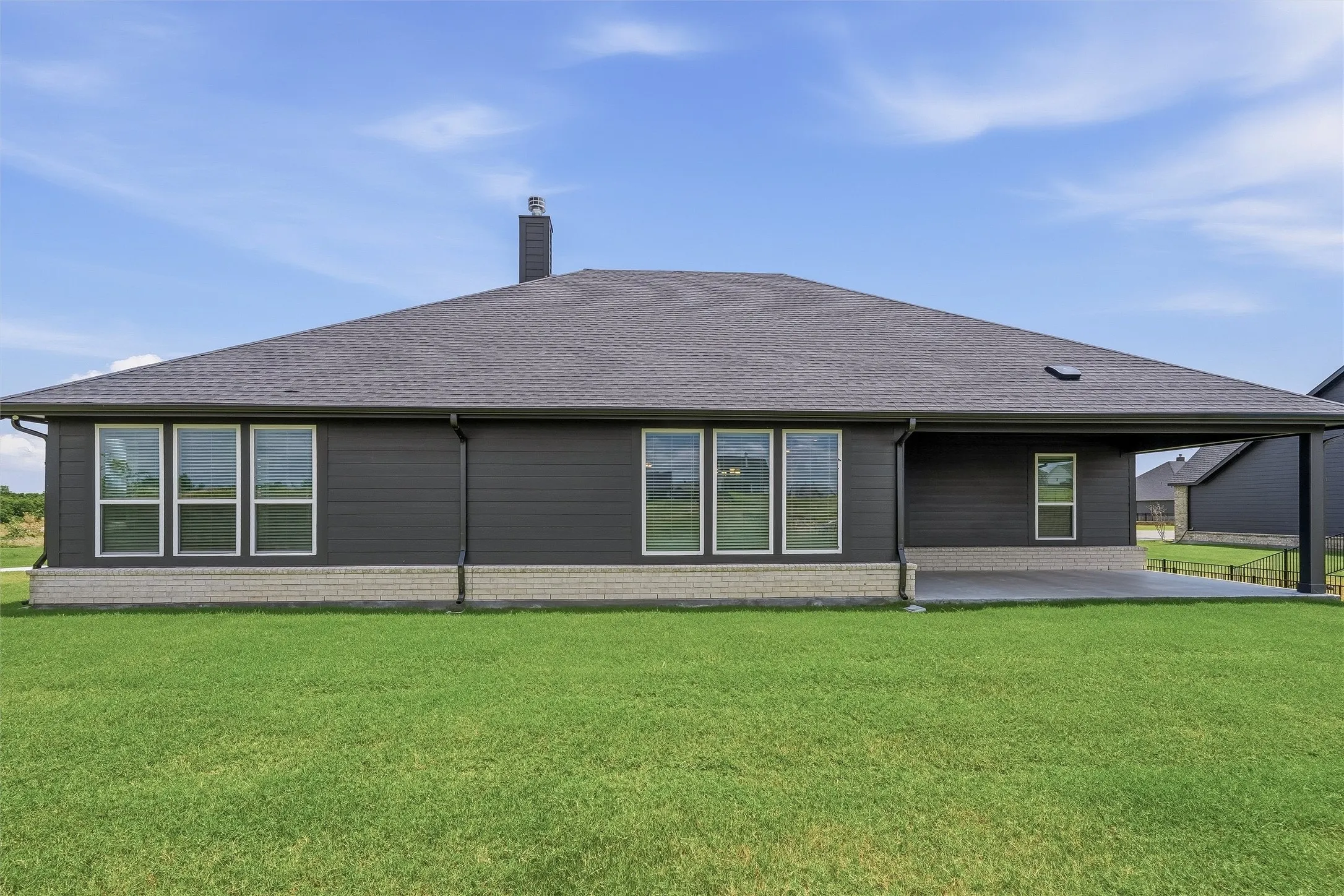 Rear exterior featuring dark siding, a light-colored brick skirt, and a covered patio with concrete flooring