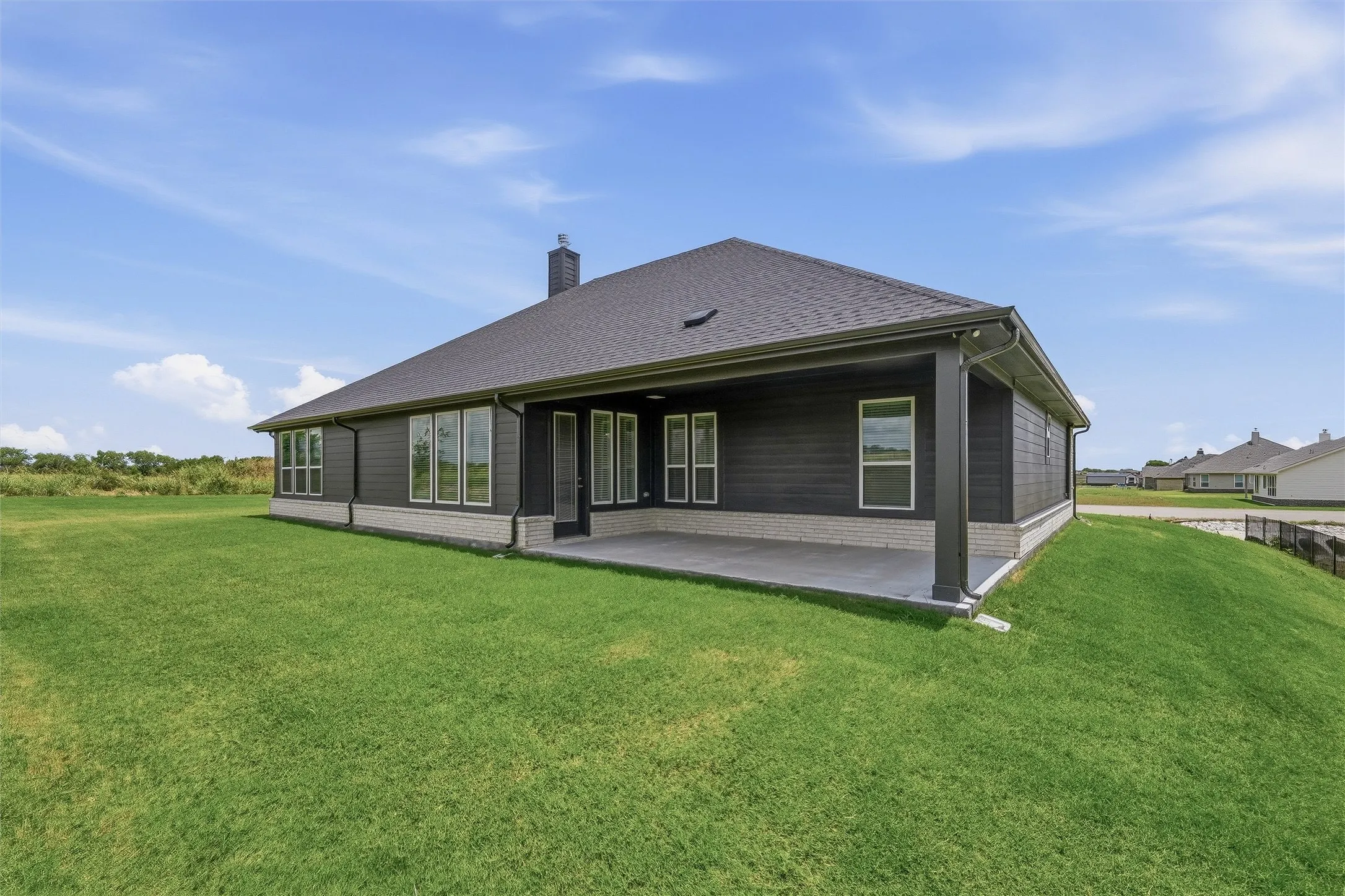 Rear exterior featuring dark horizontal siding, a dark shingle roof, and a covered concrete patio