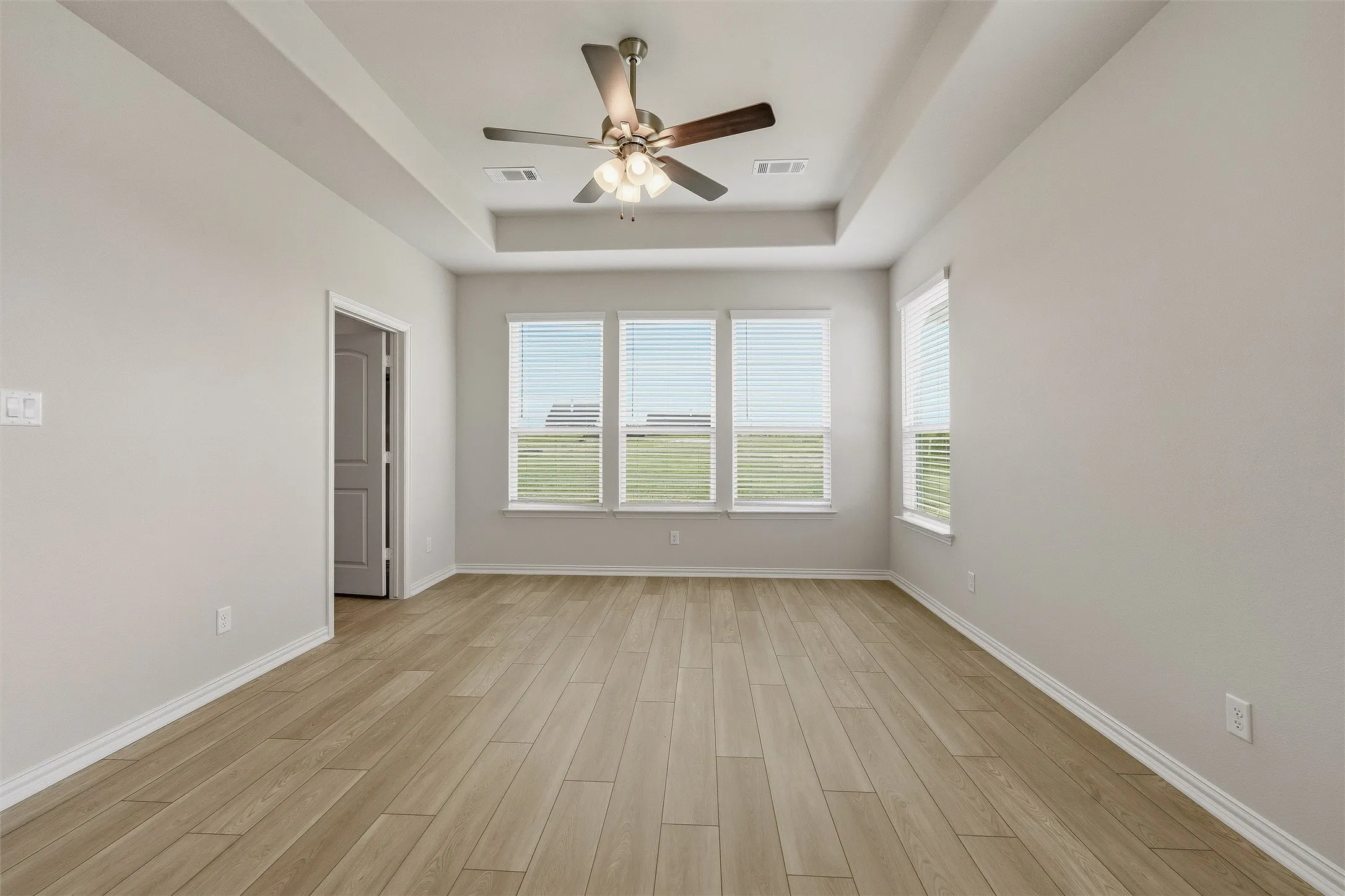 Room featuring wood-finish flooring, a tray ceiling with a ceiling fan, and multiple windows with blinds