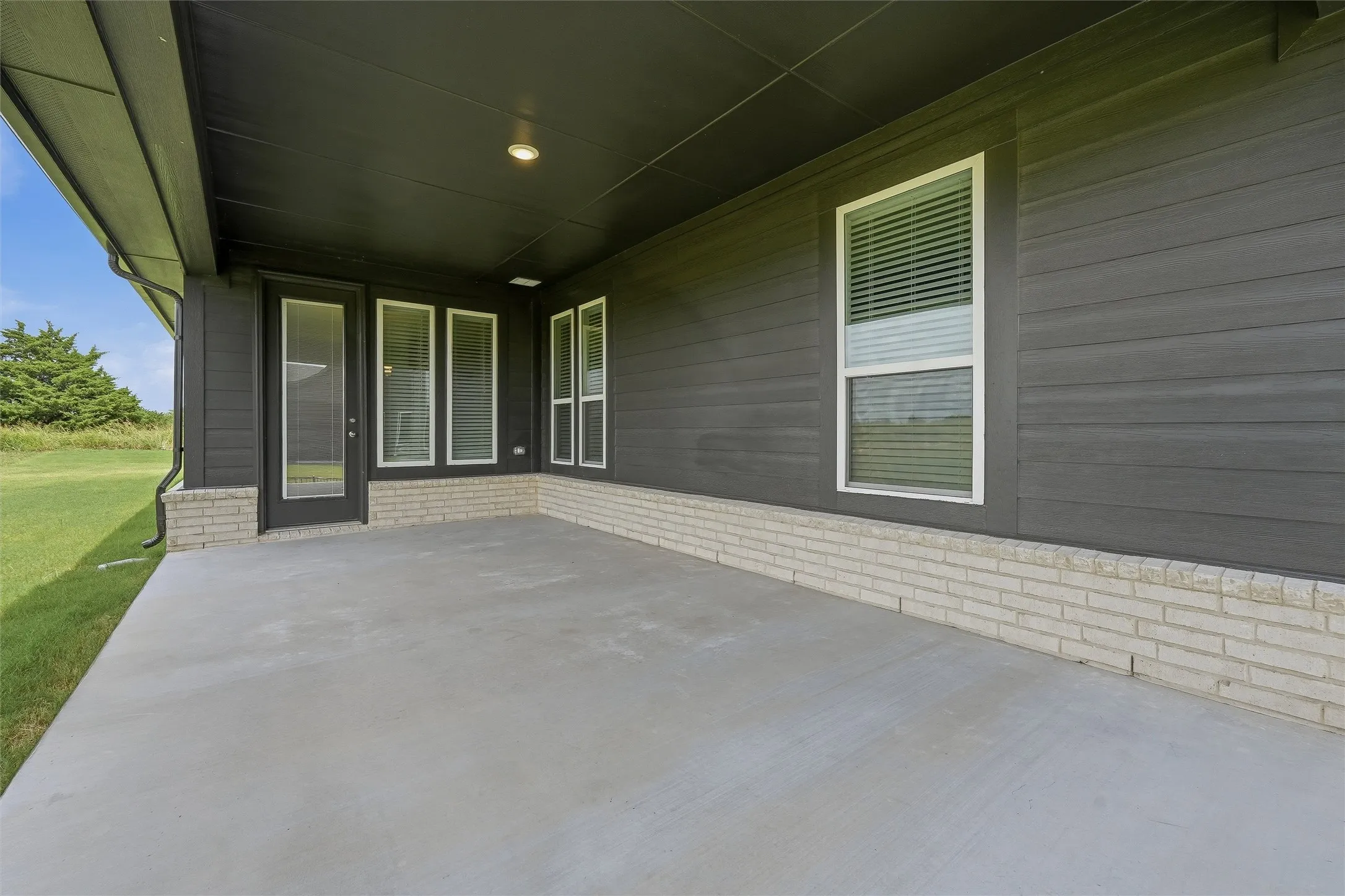 Covered concrete patio featuring a dark wood-finish exterior, white brick accents, and multiple windows
