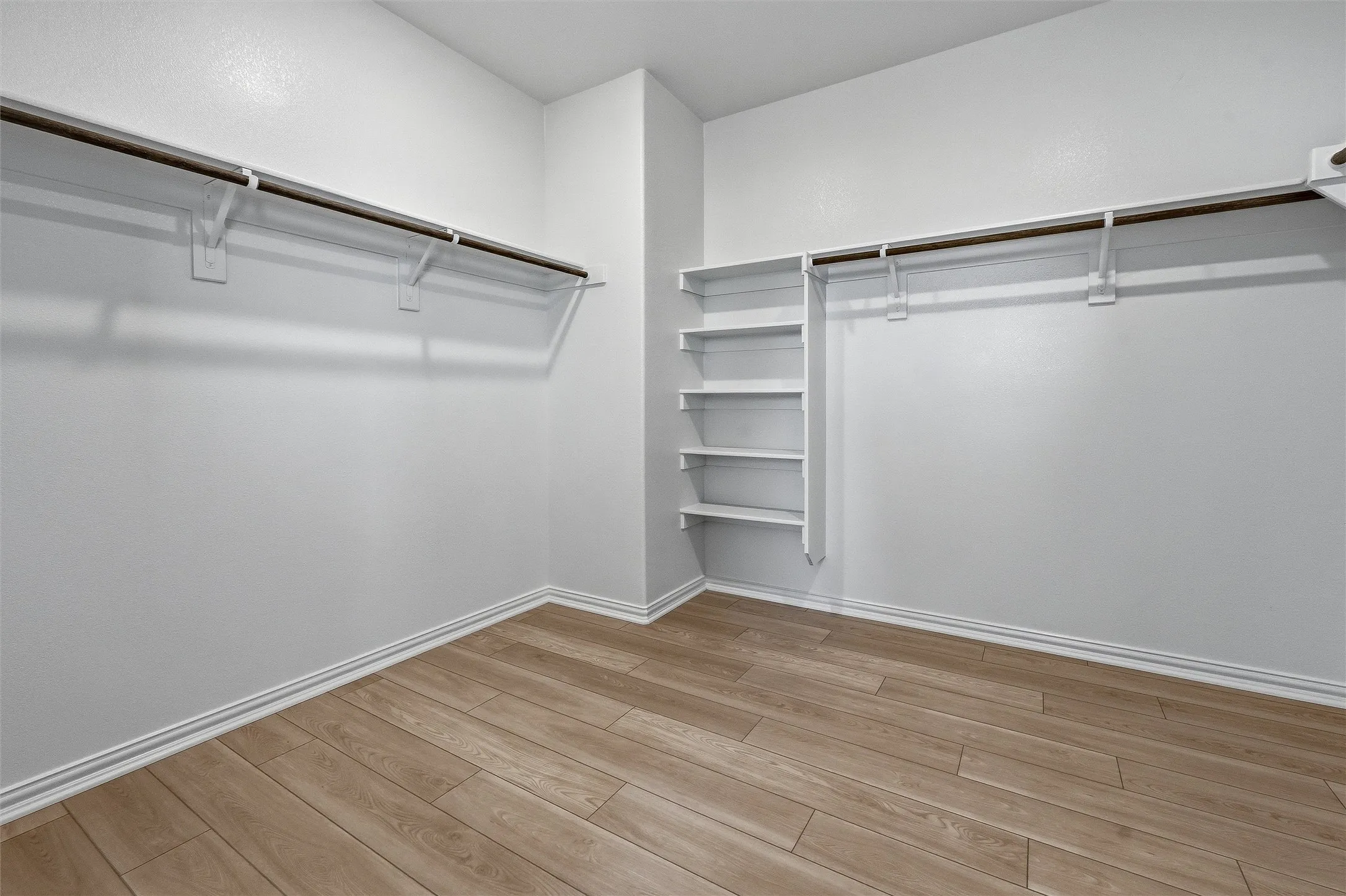 Spacious closet featuring wood-finish flooring, white walls, and white baseboards