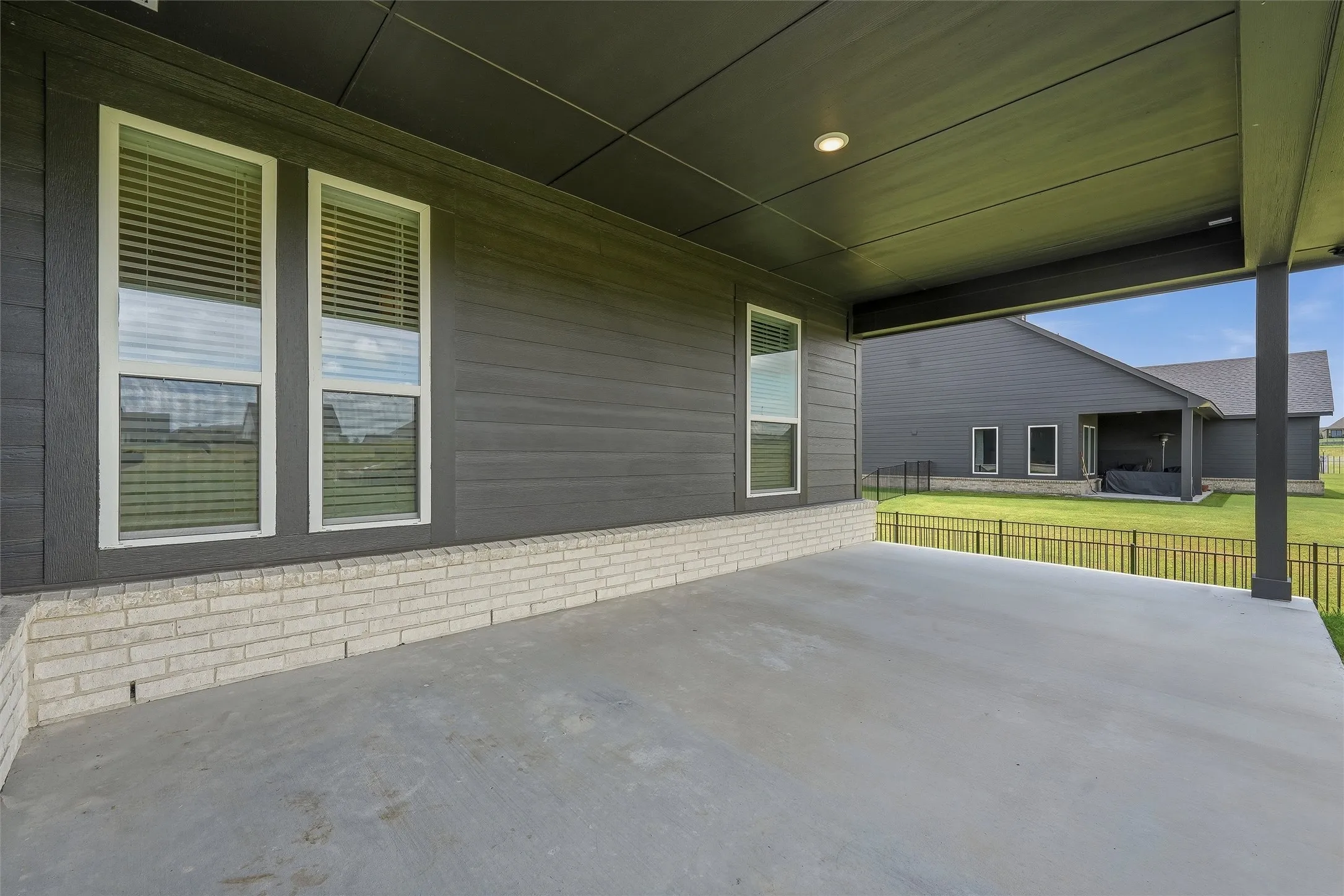 Spacious covered patio featuring a concrete surface, gray horizontal siding, and a white brick wainscoting