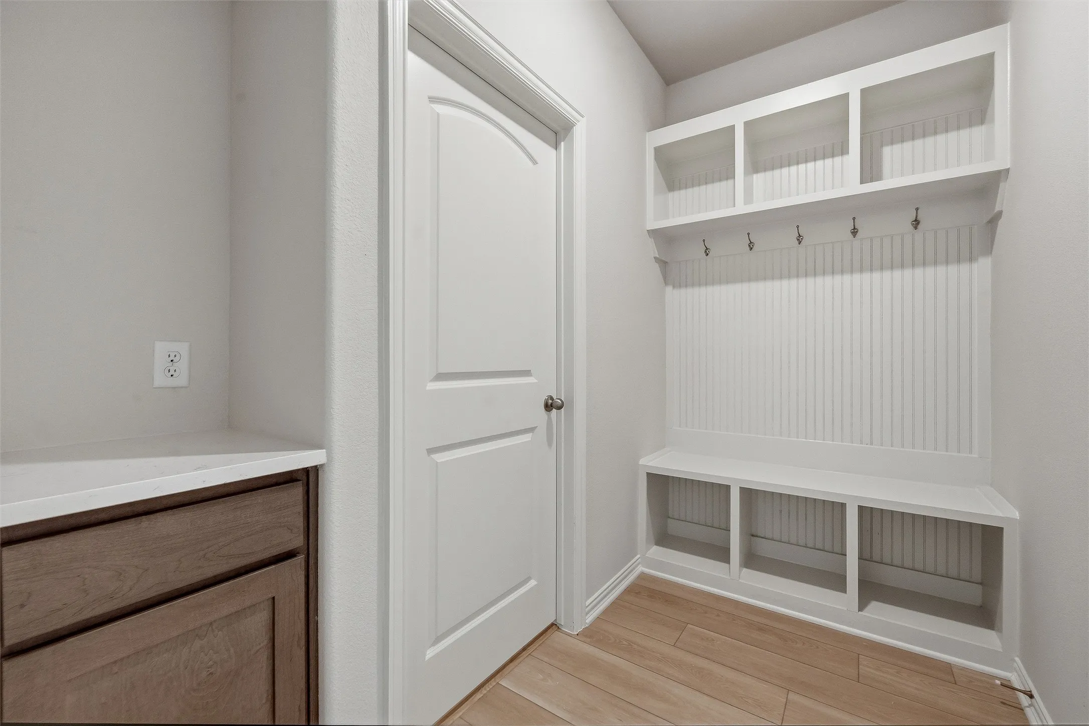 Entryway featuring built-in white shelving with hooks, a white bench with storage cubbies, and wood-finish flooring