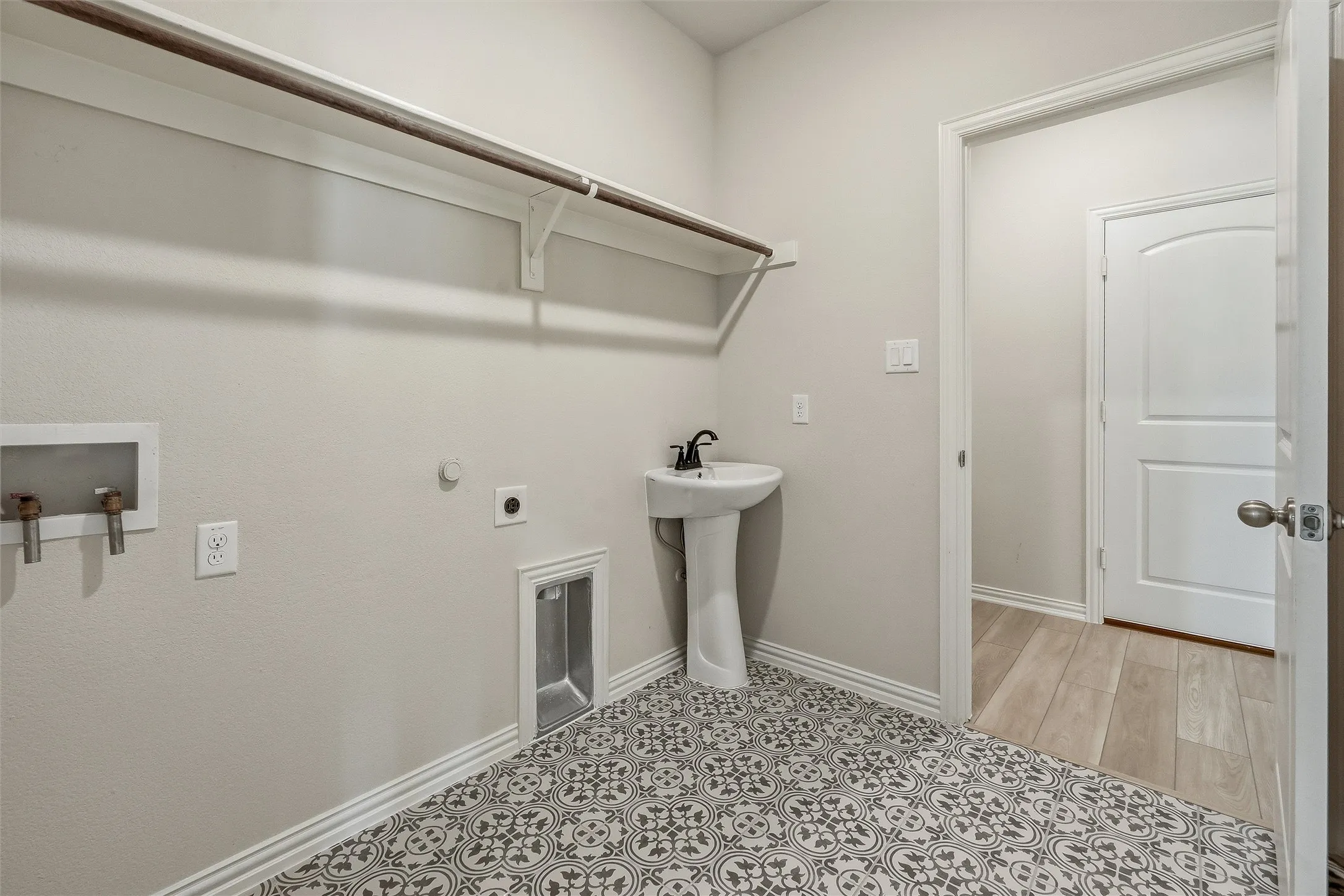 Laundry room featuring patterned floor tiles, a pedestal sink with a matte black faucet, and a wall-mounted clothing rod