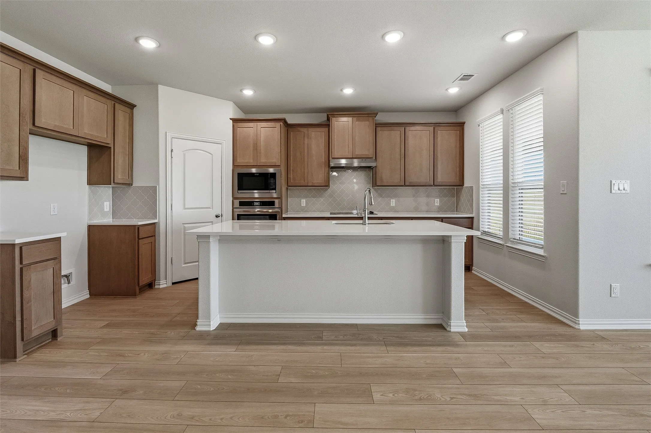 Kitchen featuring a central island with a solid surface countertop, wood-finish flooring, recessed lighting, stainless steel appliances, and multiple windows with blinds