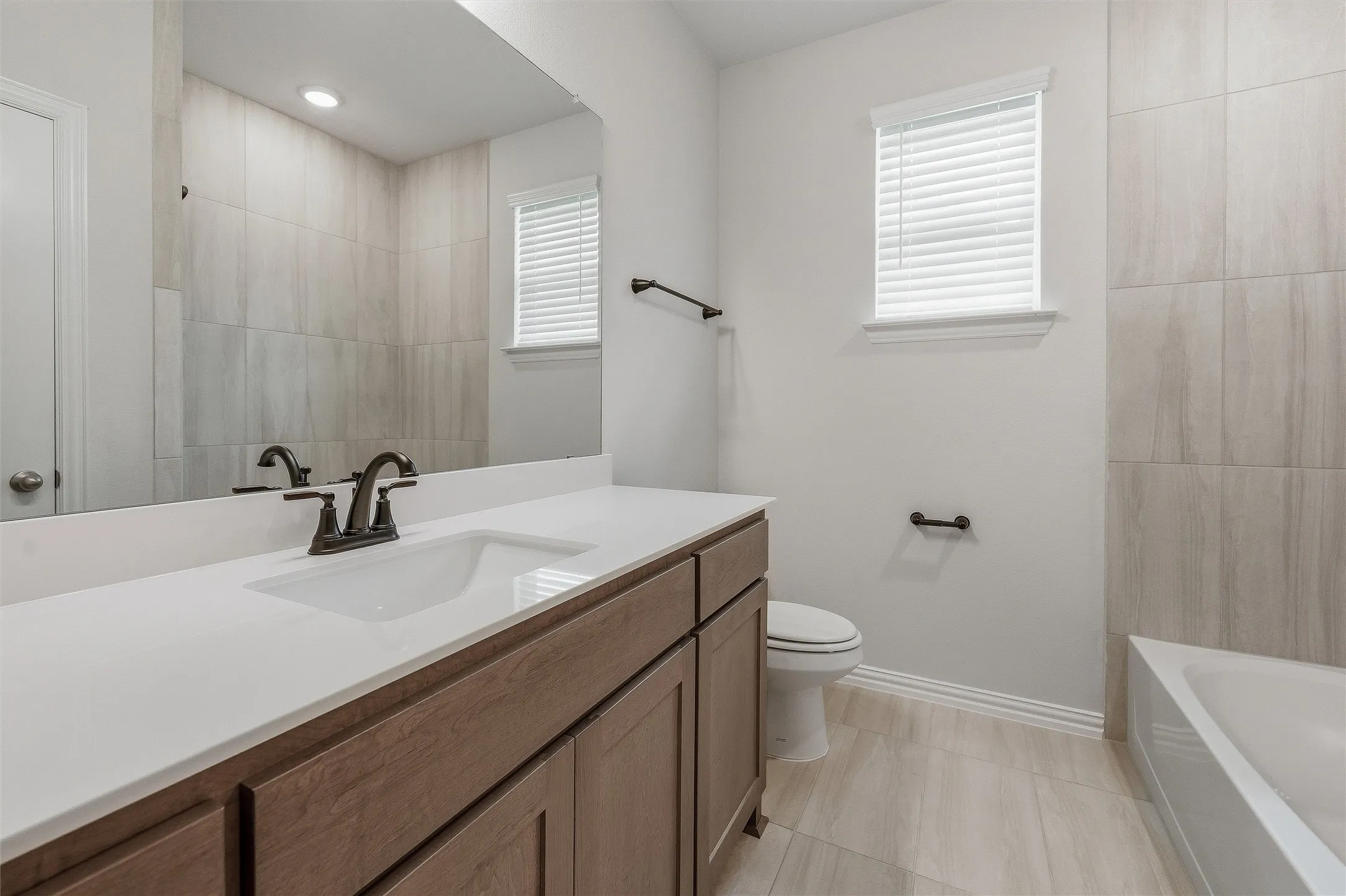 White countertop vanity with dark wood-finish cabinetry, a large wall-mounted mirror, and a modern bronze-finish faucet