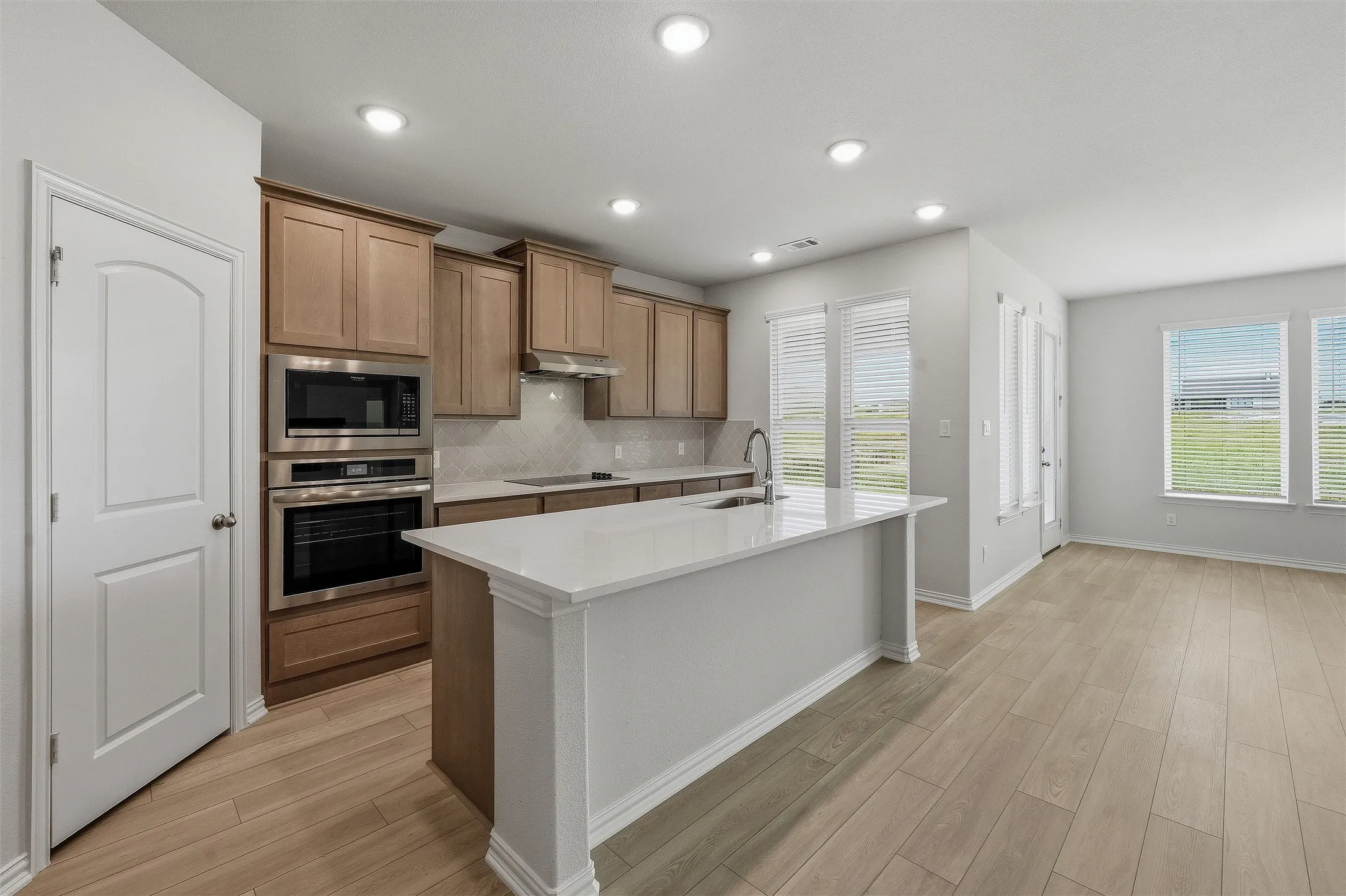 Modern kitchen featuring an island with an undermount sink, stainless steel appliances, wood-finish flooring, recessed lighting, and ample natural light from multiple windows
