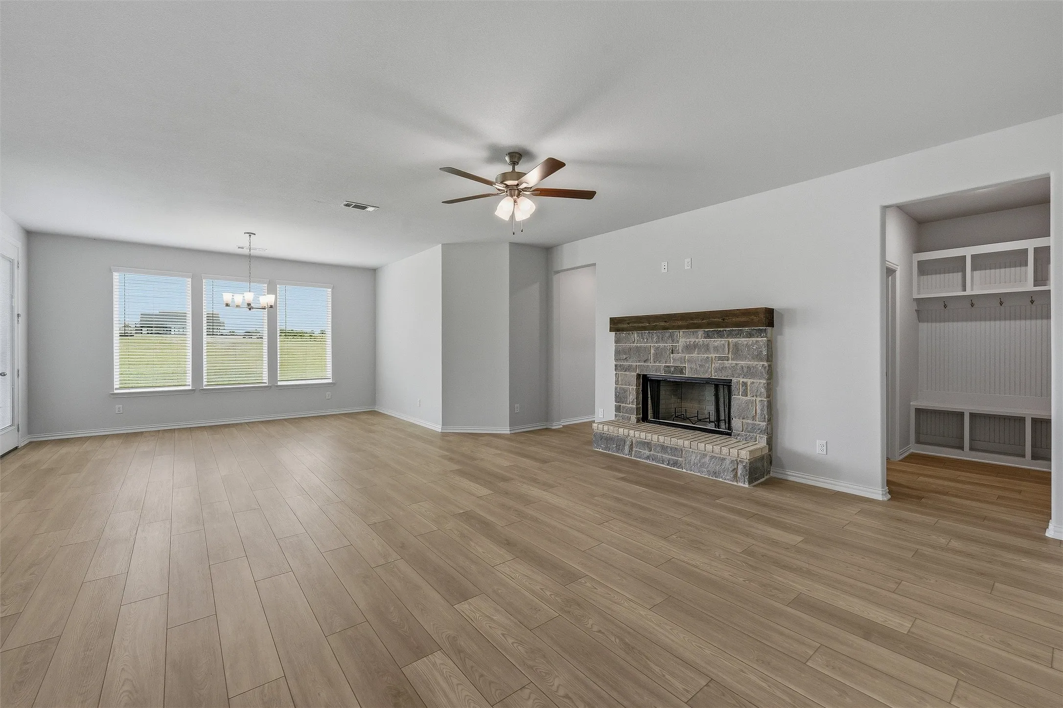 Spacious living area featuring light wood-finish flooring, a stone fireplace with a wood-beam mantel, and a built-in mudroom bench with storage and coat hooks