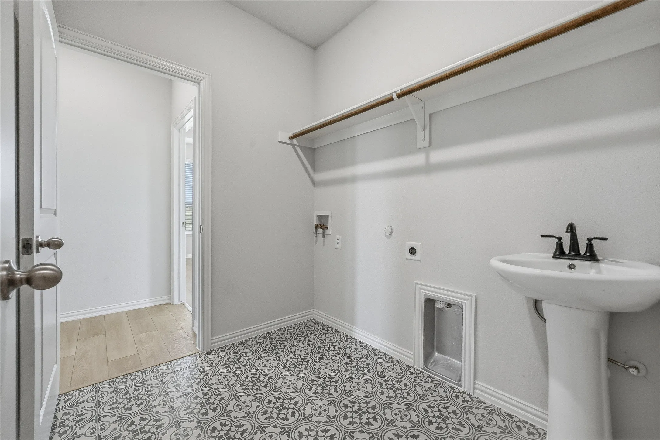 Utility room featuring patterned floor tile, a pedestal sink with a matte black faucet, and a built-in hanging rod with shelving