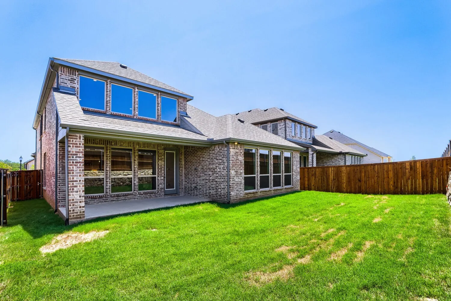 Spacious backyard featuring a covered concrete patio, full privacy fencing, and a brick exterior with multiple windows