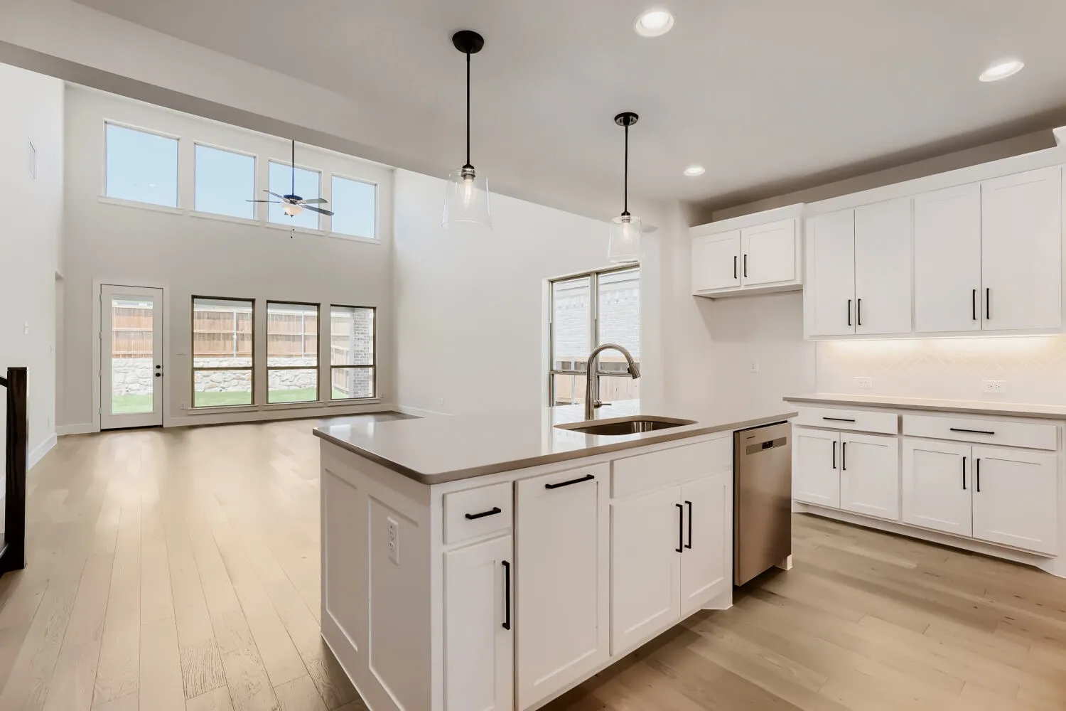 Modern kitchen featuring an island with an undermount sink and stainless steel faucet, white shaker cabinetry, light-toned countertops, and wood-finish flooring