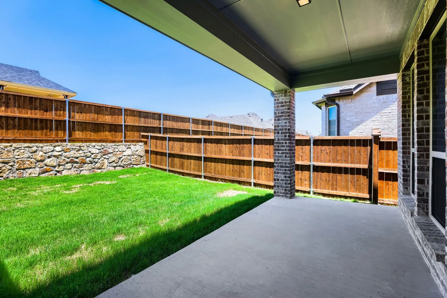 Covered patio area with concrete flooring, brick columns, and recessed lighting