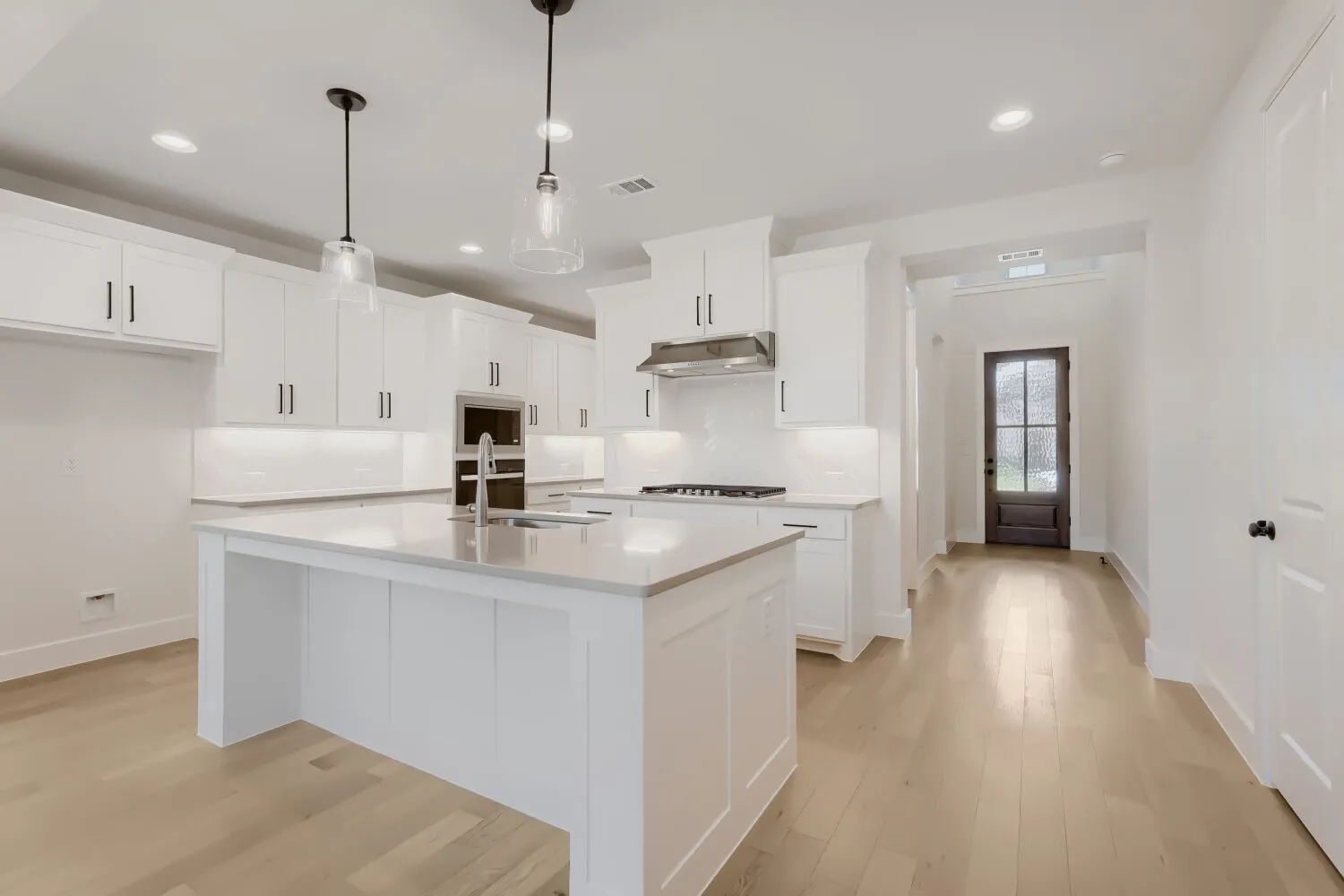 Gourmet kitchen featuring a central island with integrated sink, white cabinetry with dark hardware, built-in stainless steel appliances, and wood-finish flooring