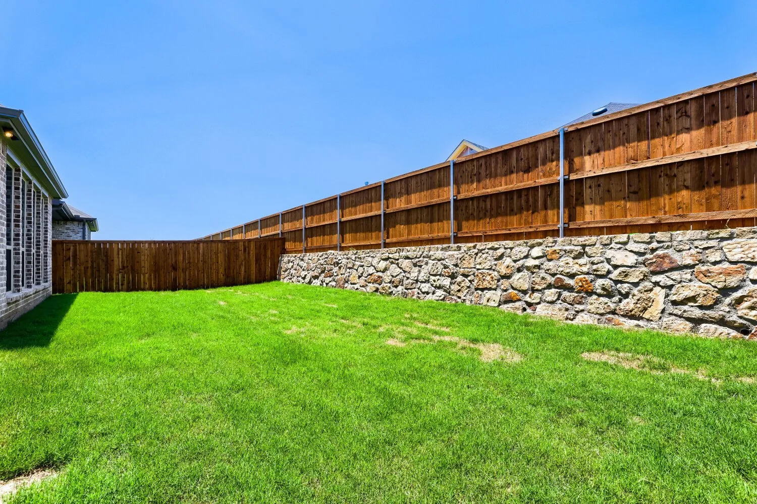 Expansive backyard featuring a lush lawn, a full wood privacy fence, and a stone retaining wall
