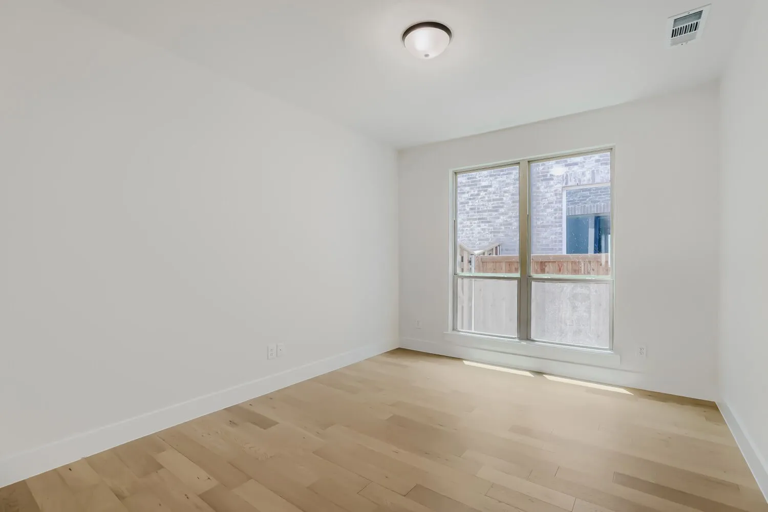 Spacious room featuring wood-finish flooring, white baseboards, and a large window