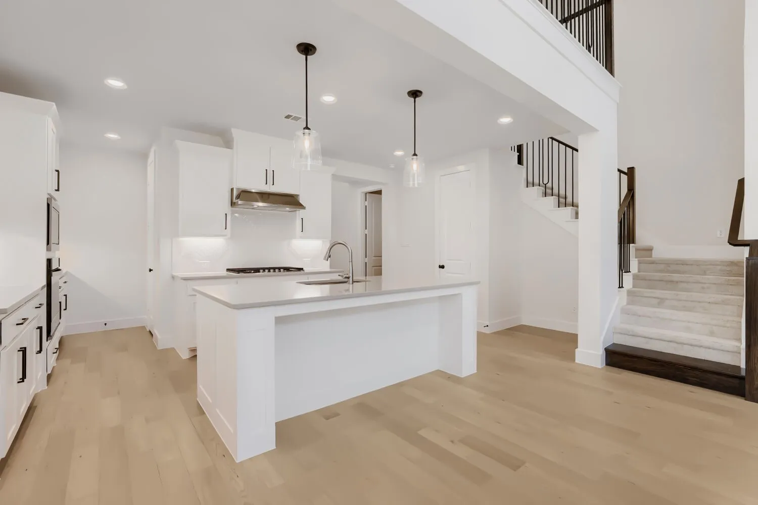 Open-concept kitchen featuring white cabinetry, light-toned wood-finish flooring, a central island with integrated sink, stainless steel appliances, and quartz countertops