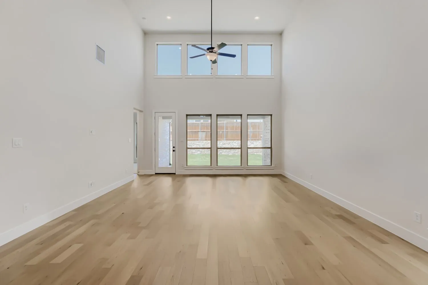 Expansive open-concept living space featuring high ceilings, wood-finish flooring, and abundant natural light from multiple windows