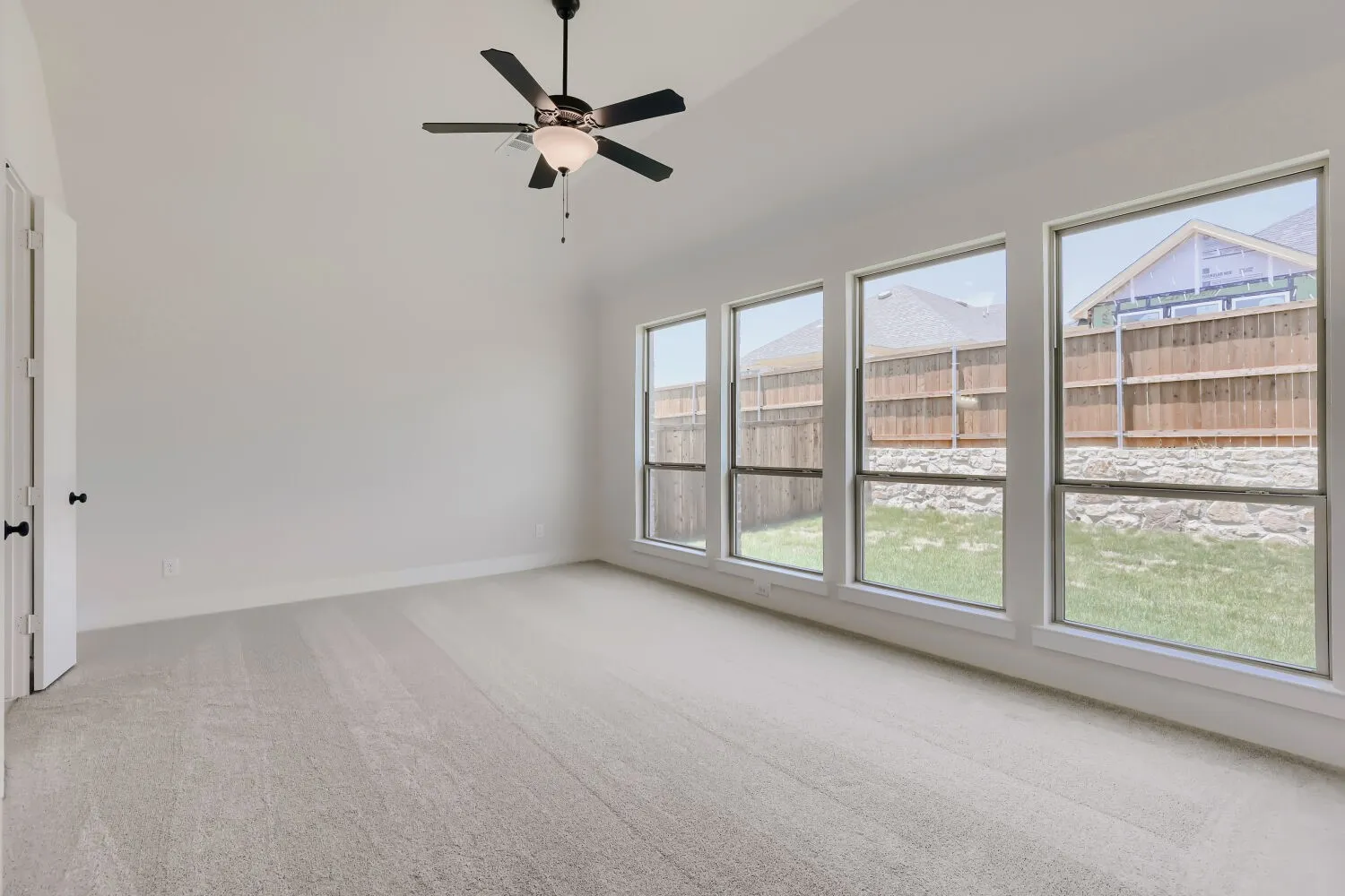 Spacious room featuring vaulted ceilings, light-colored carpeting, and a modern ceiling fan