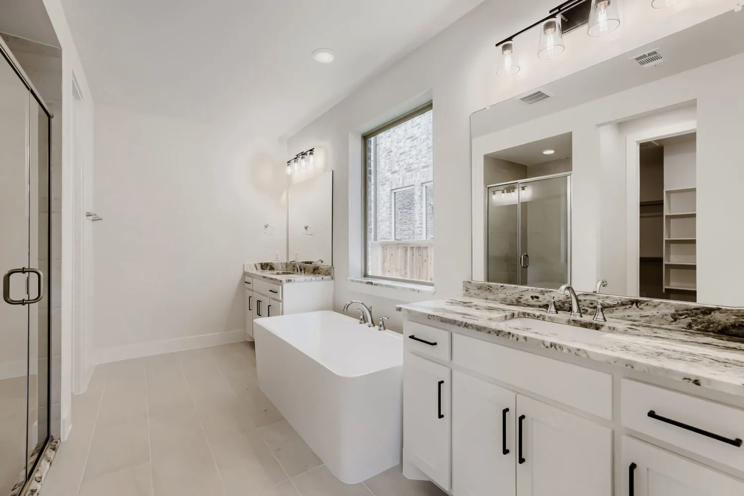 Contemporary bathroom featuring a freestanding tub, dual vanities with stone countertops, a glass-enclosed shower, and built-in shelving