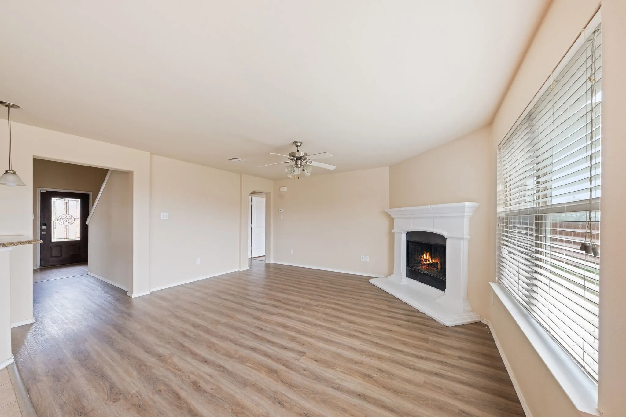 Unfurnished living room featuring a lit fireplace, light wood-type flooring, and ceiling fan
