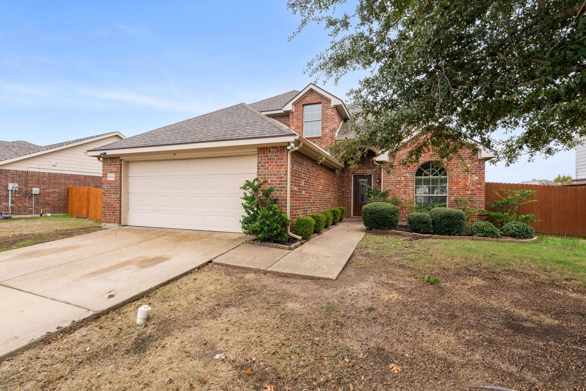 Traditional-style home featuring driveway, brick siding, roof with shingles, and an attached garage